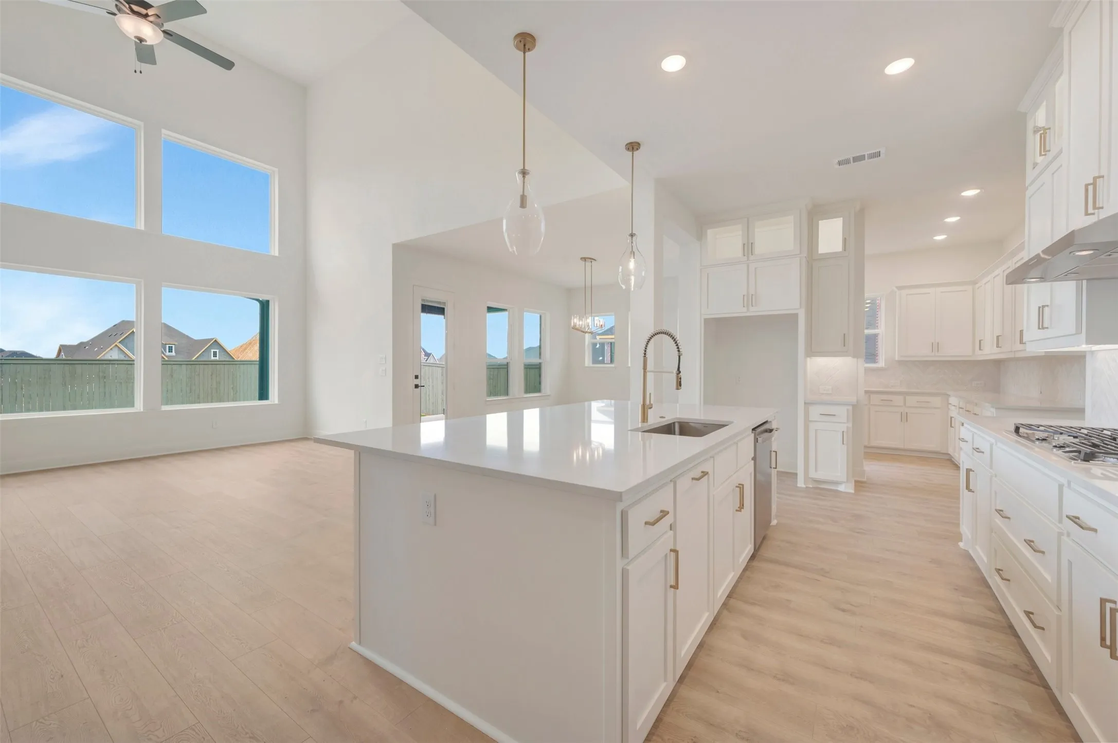Open-concept living space featuring a kitchen island with sink and stainless steel dishwasher, white cabinetry with gold-finish hardware, recessed lighting, and wood-finish flooring