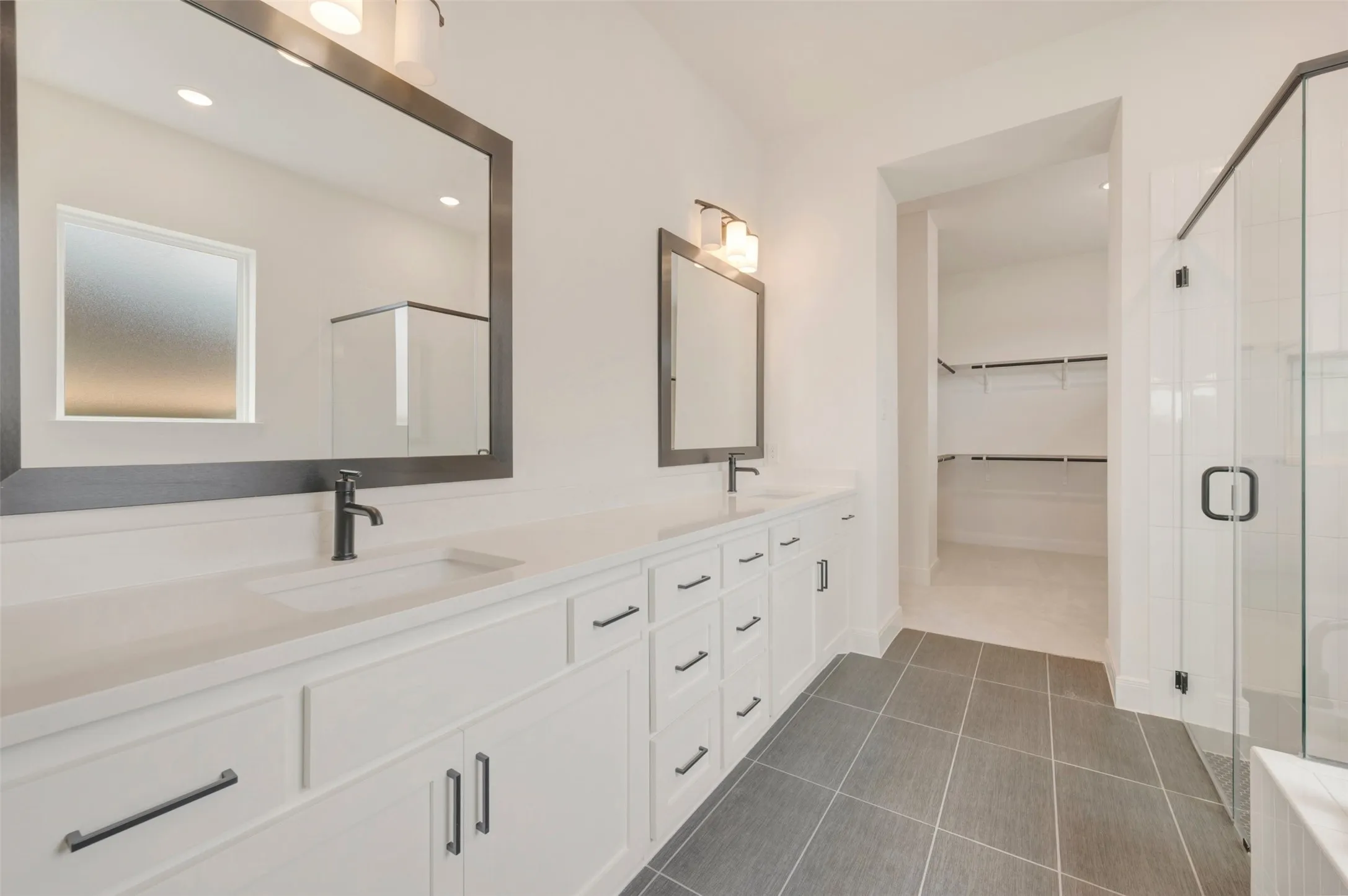 Contemporary bathroom featuring a double vanity with white cabinetry, matte black hardware, and an expansive countertop