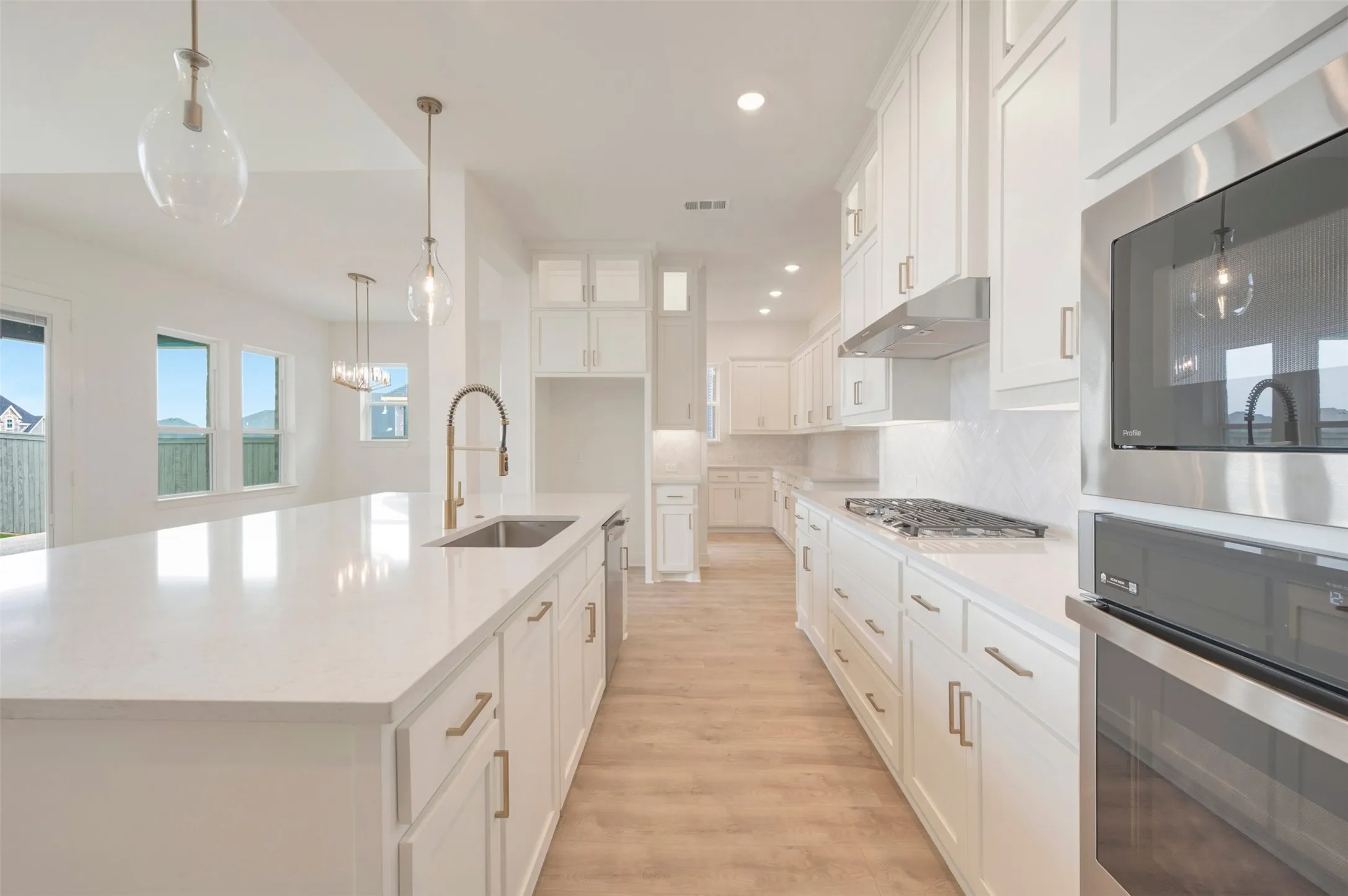 Modern kitchen featuring white cabinetry, light countertops, wood-finish flooring, a kitchen island with an undermount sink, and stainless steel appliances