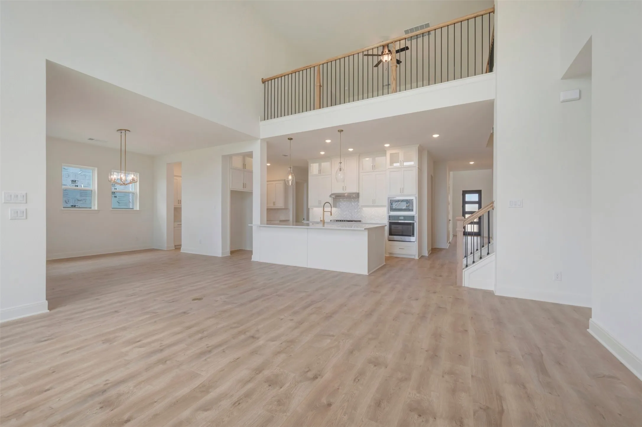 Spacious interior featuring wood-finish flooring, a two-story ceiling, and an open-concept kitchen with white cabinetry and an island