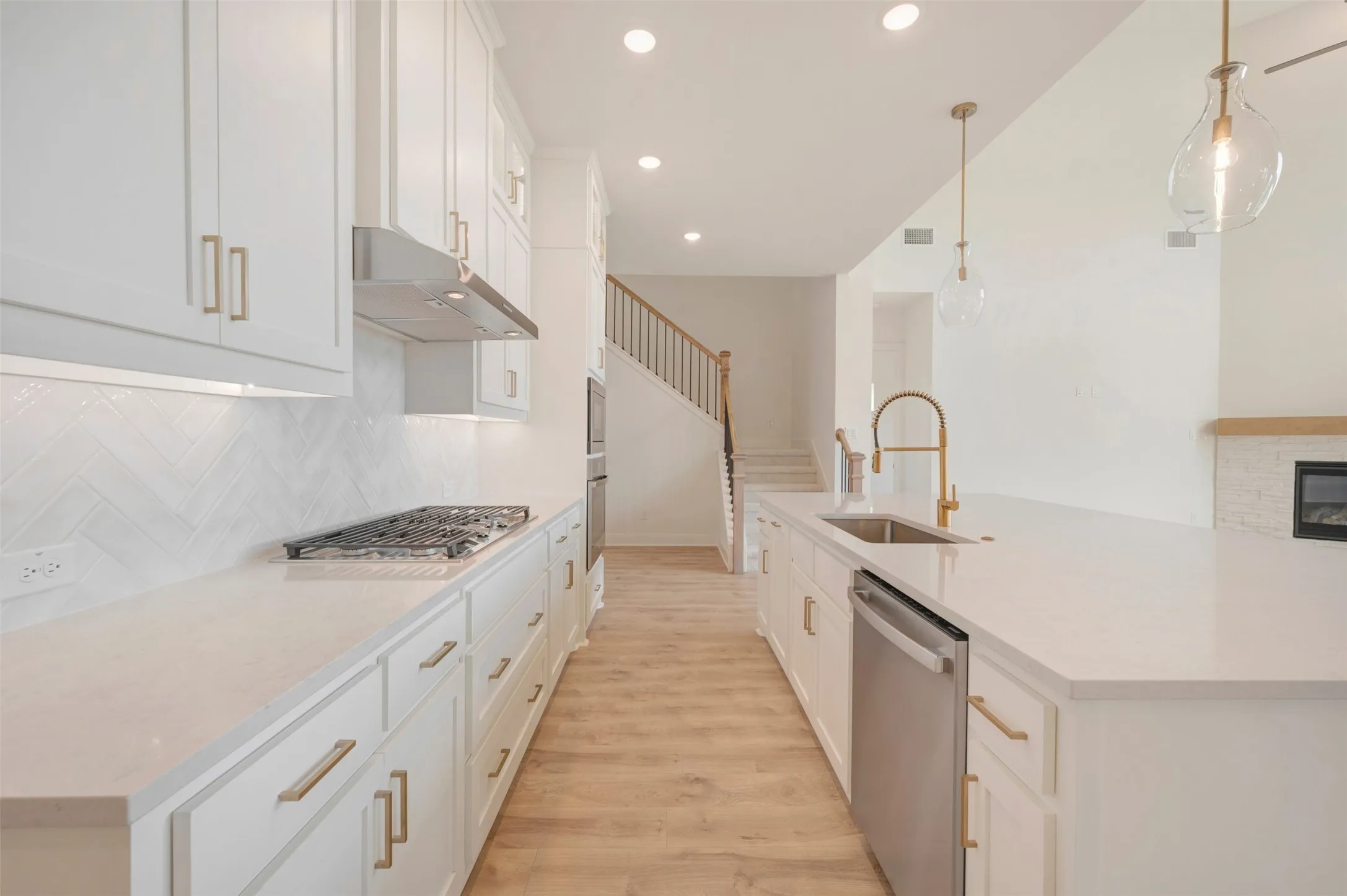 Contemporary kitchen featuring white cabinetry with brass hardware, a gas range with stainless steel hood, and a herringbone tile backsplash