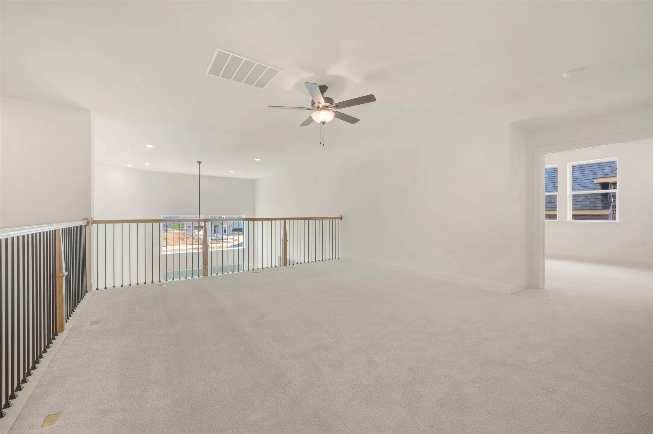 Spacious upper-level area featuring light-colored carpeting, a ceiling fan with integrated lighting, recessed lighting, a white painted ceiling, and a doorway leading to a separate room with windows