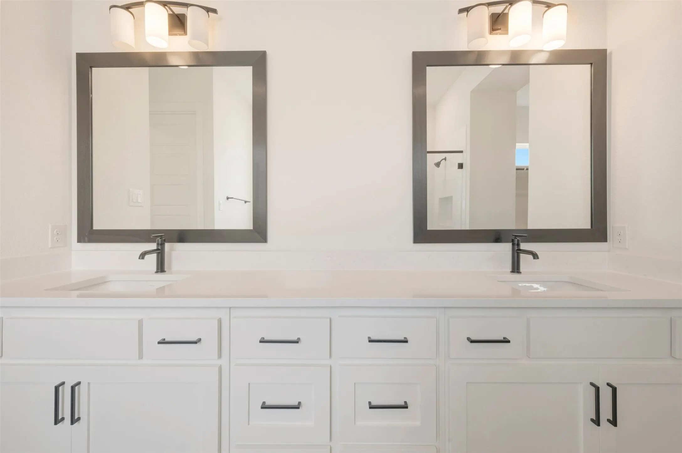 Dual vanities featuring white cabinetry with matte black hardware, integrated sinks, and light-toned countertops