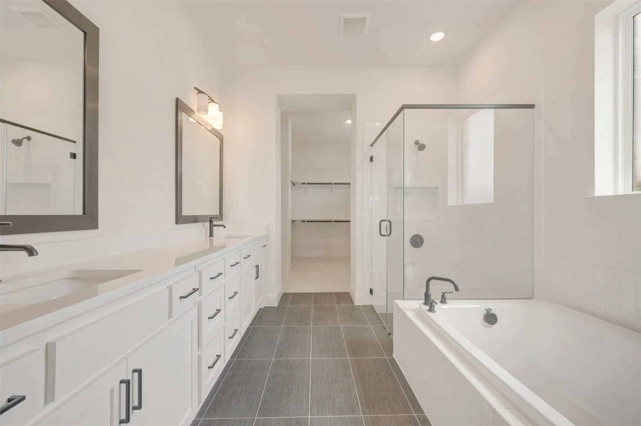 Contemporary bathroom featuring a double vanity with stone countertops, a freestanding bathtub, and a glass-enclosed shower