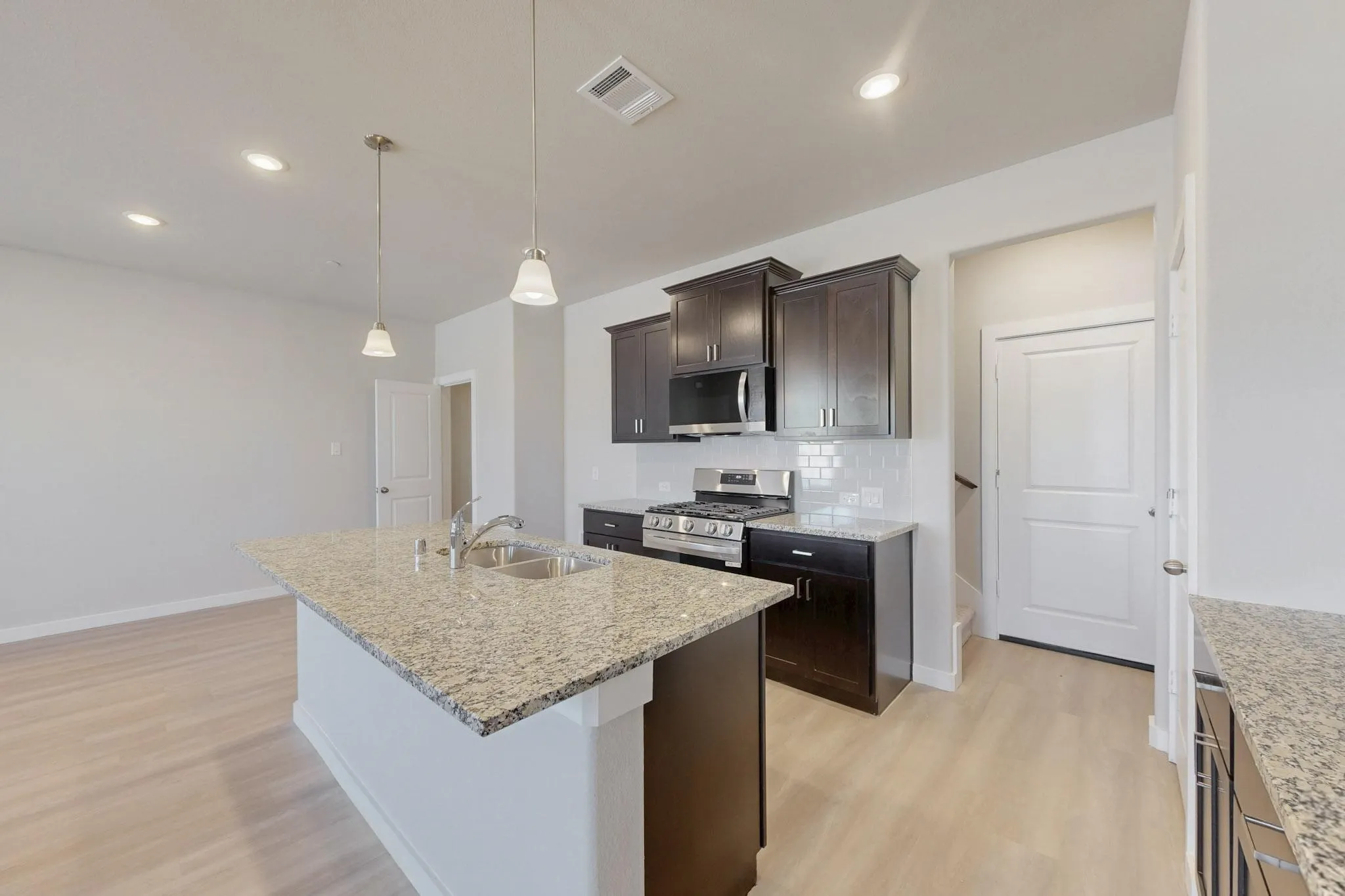 Kitchen featuring stainless steel appliances, dark brown cabinets, tasteful backsplash, light wood-style flooring, and hanging light fixtures