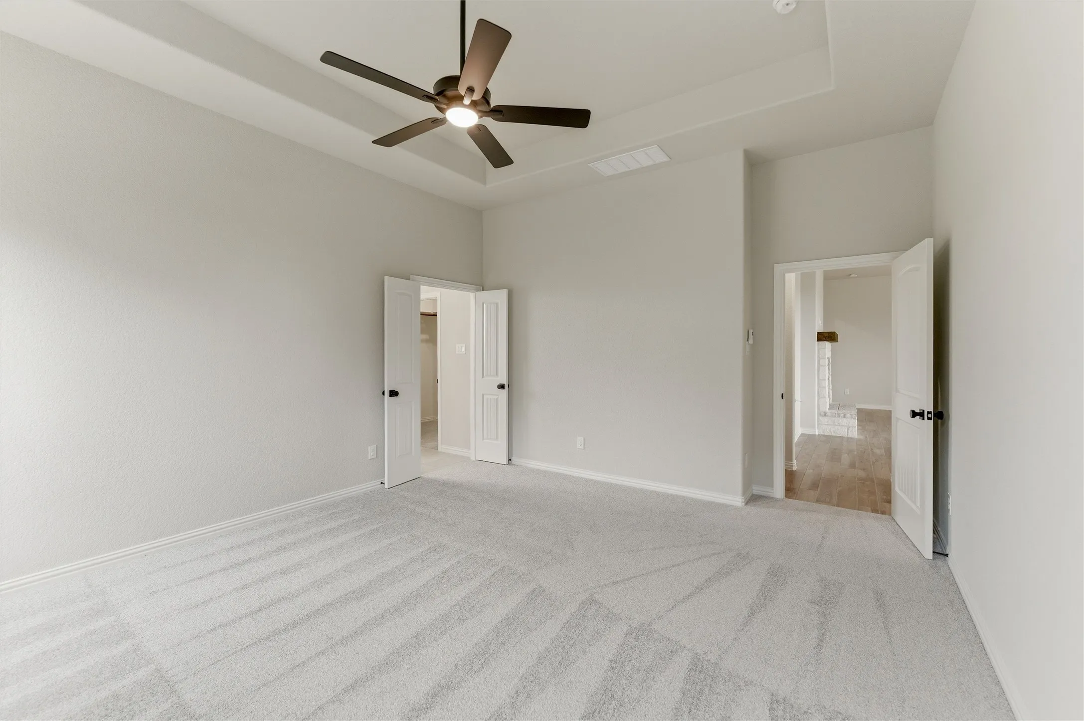 Unfurnished bedroom featuring a tray ceiling, a ceiling fan, light carpet, and ensuite bathroom