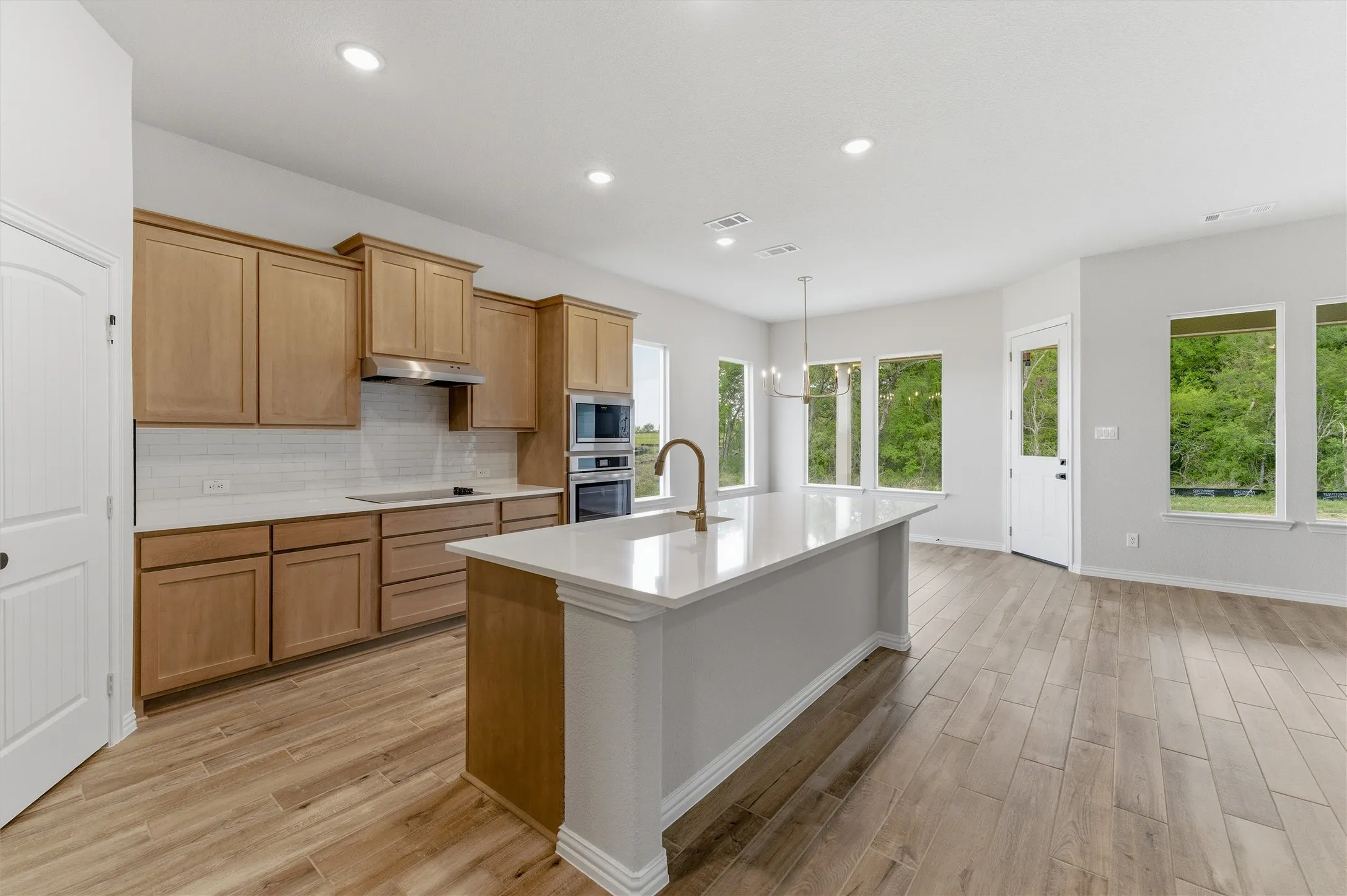 Kitchen with light wood-type flooring, a kitchen island with sink, decorative backsplash, stainless steel appliances, and light stone counters