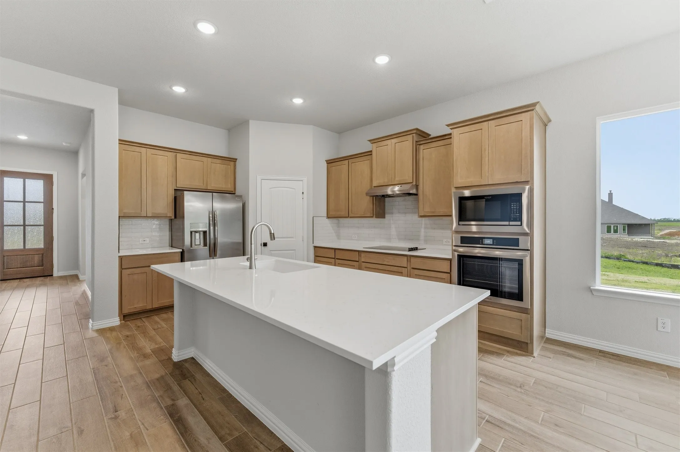 Kitchen featuring stainless steel appliances, an island with sink, decorative backsplash, light wood-style floors, and recessed lighting