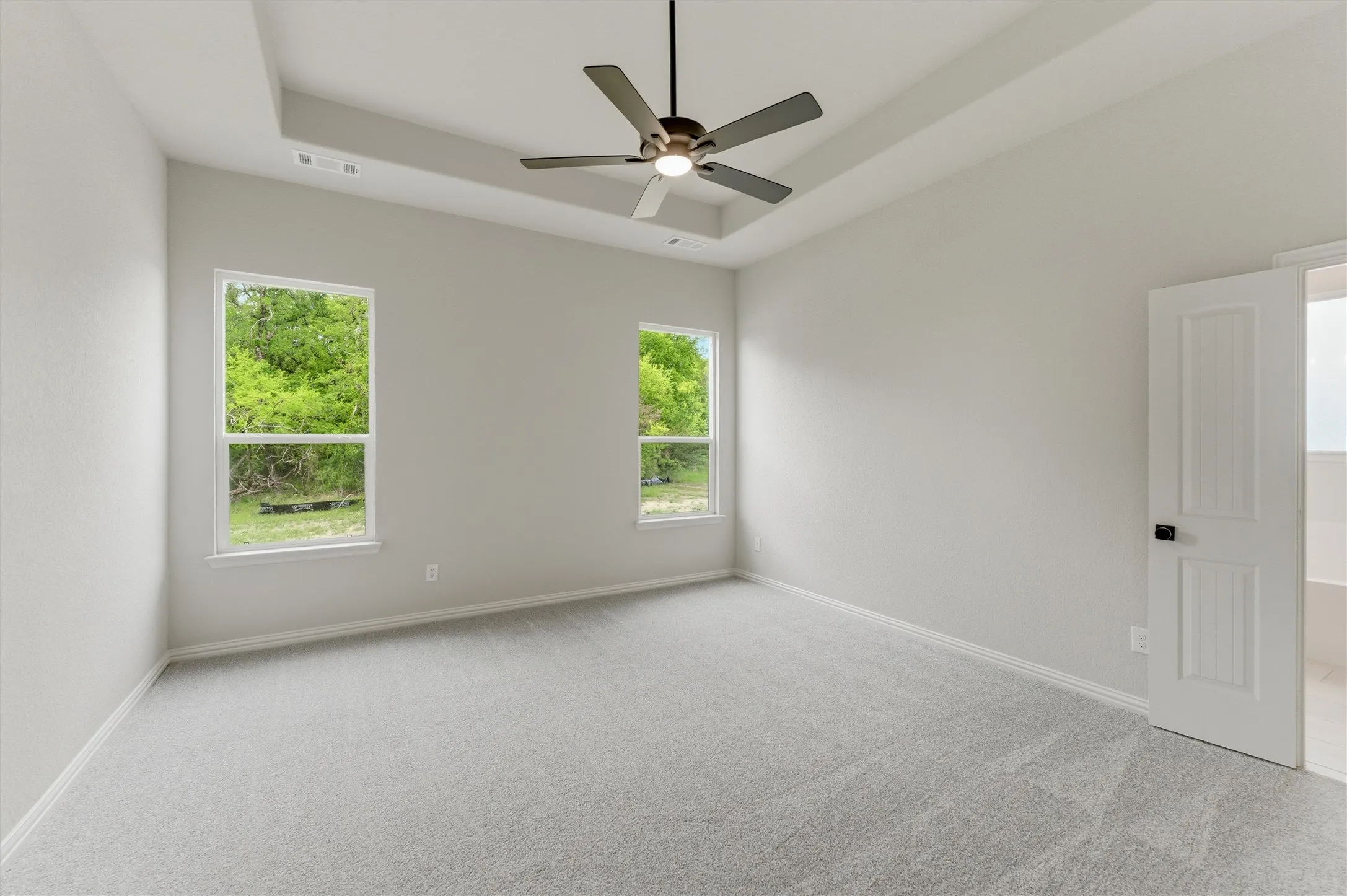 Unfurnished room featuring light carpet, a tray ceiling, and ceiling fan