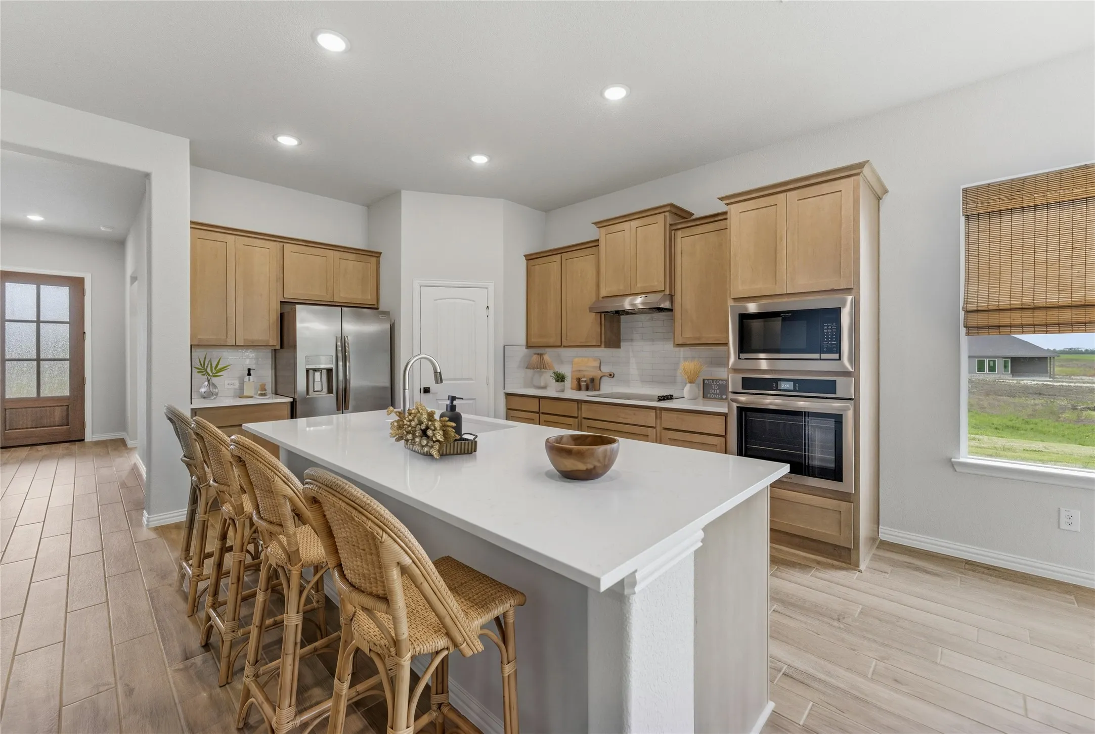 Kitchen featuring a large central island with seating, stainless steel appliances, light wood-finish cabinetry, recessed lighting, and wood-finish flooring