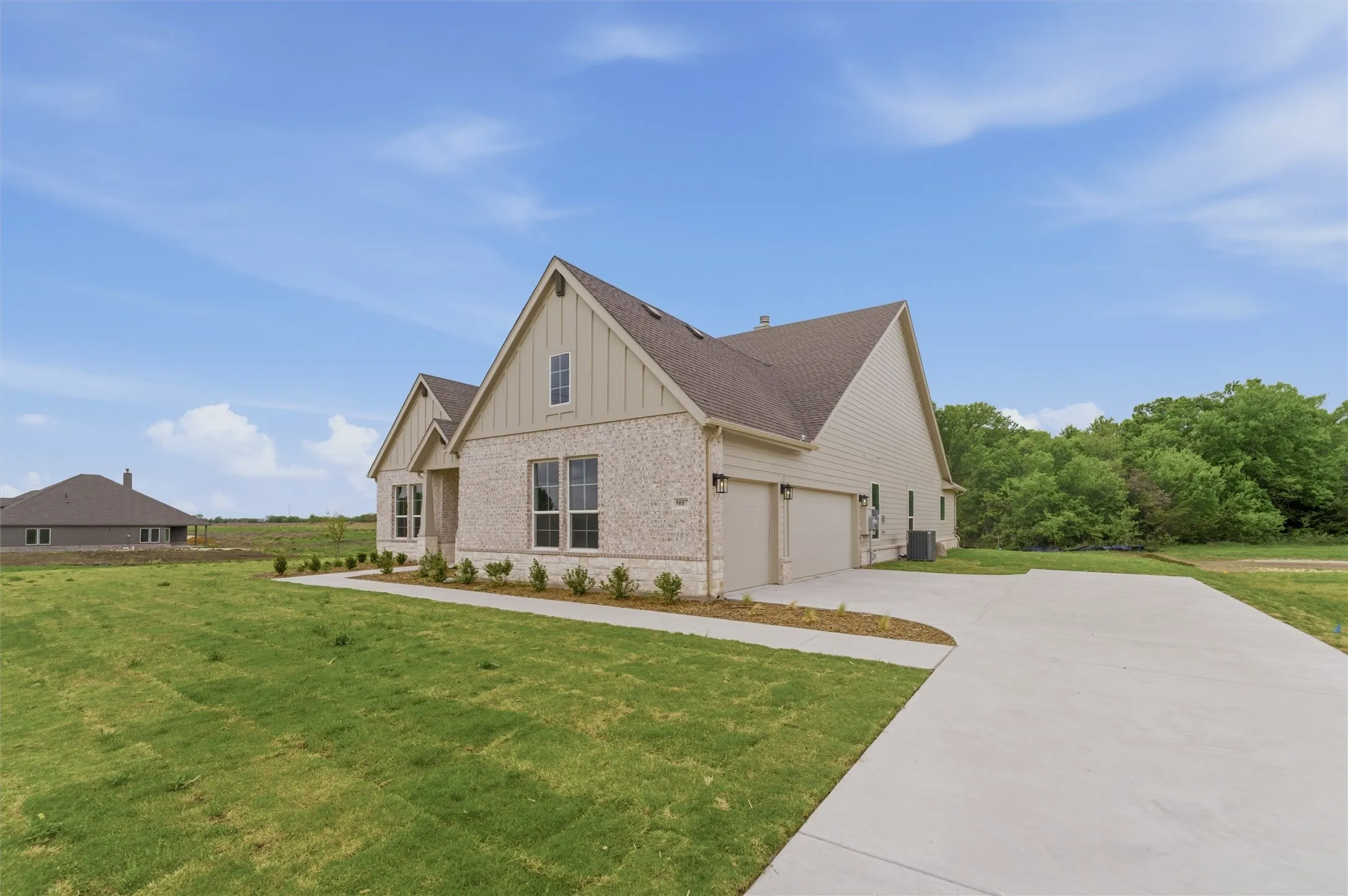 View of property exterior with board and batten siding, brick siding, a lawn, and concrete driveway
