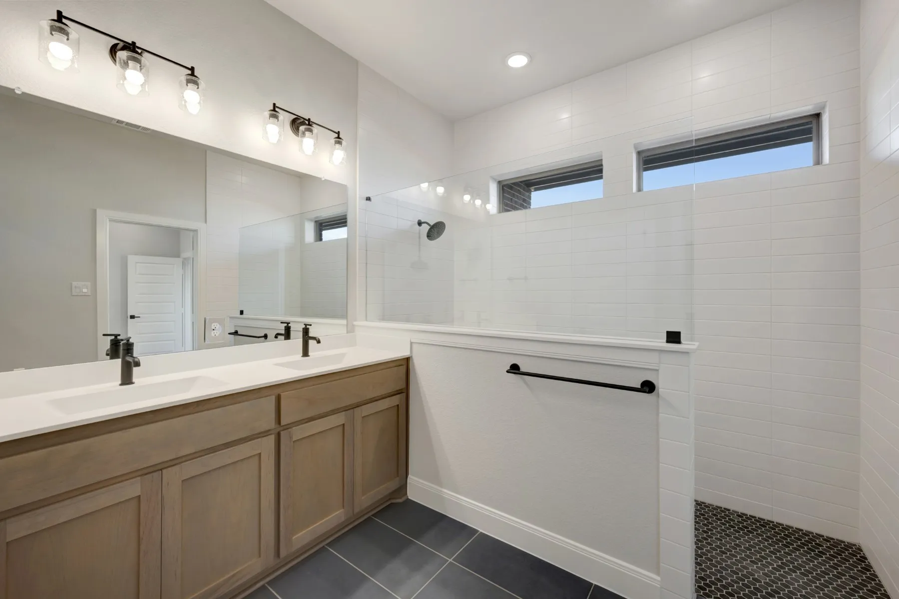 Bathroom with double vanity, a walk in shower, and dark tile patterned floors
