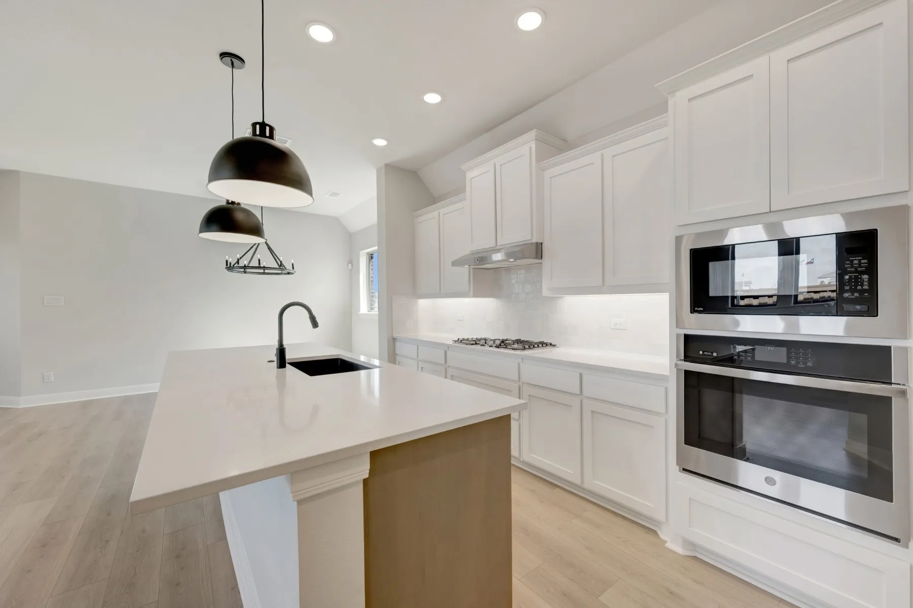 Kitchen with white cabinetry, stainless steel appliances, an island with sink, light wood finished floors, and vaulted ceiling