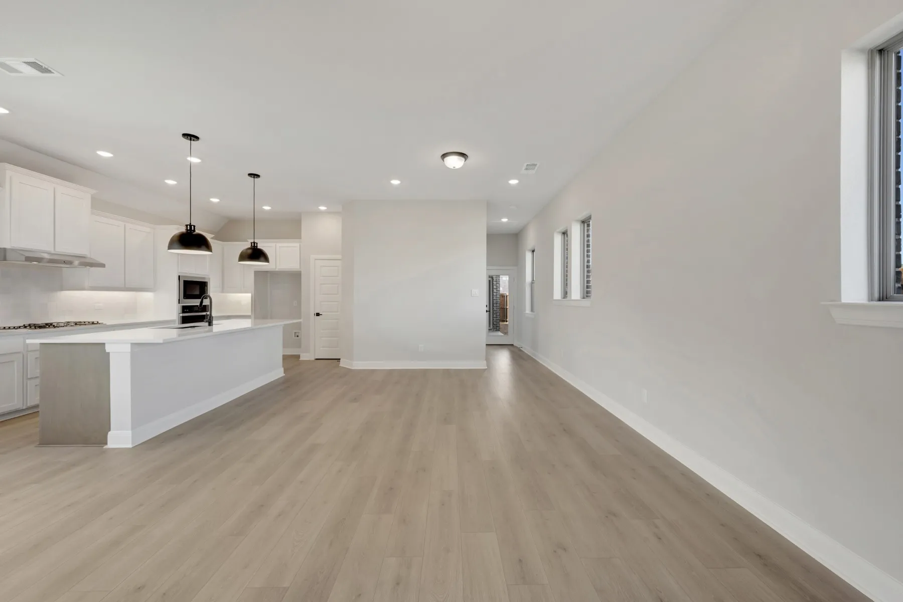Kitchen with white cabinets, light wood-style flooring, a center island with sink, open floor plan, and decorative light fixtures