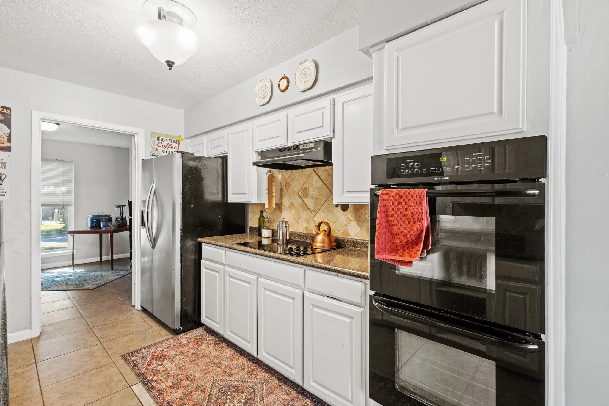 Kitchen featuring black appliances, white cabinetry, tasteful backsplash, light tile patterned flooring, and a textured ceiling