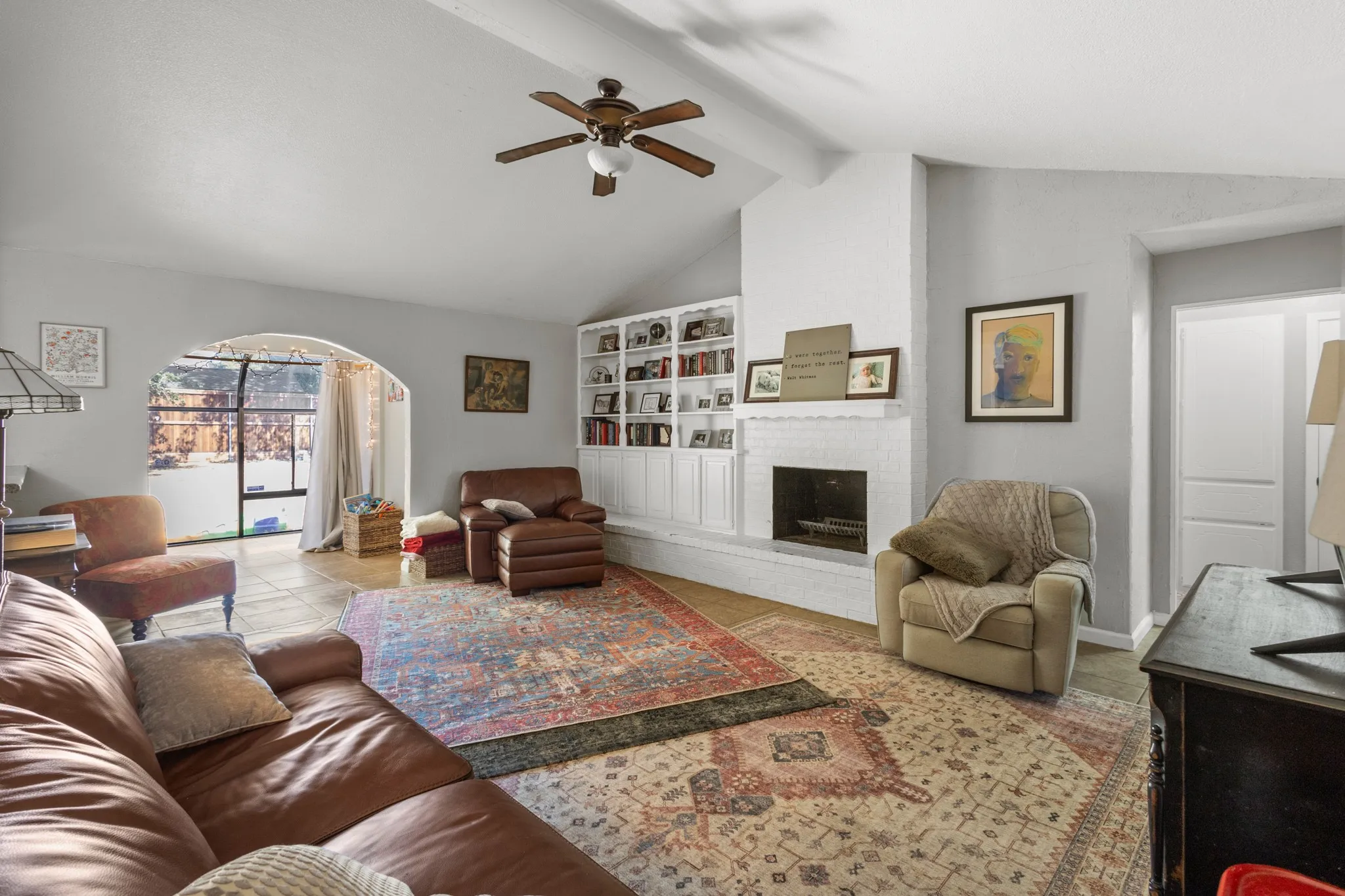 Living area featuring a ceiling fan, a brick fireplace, and arched walkways