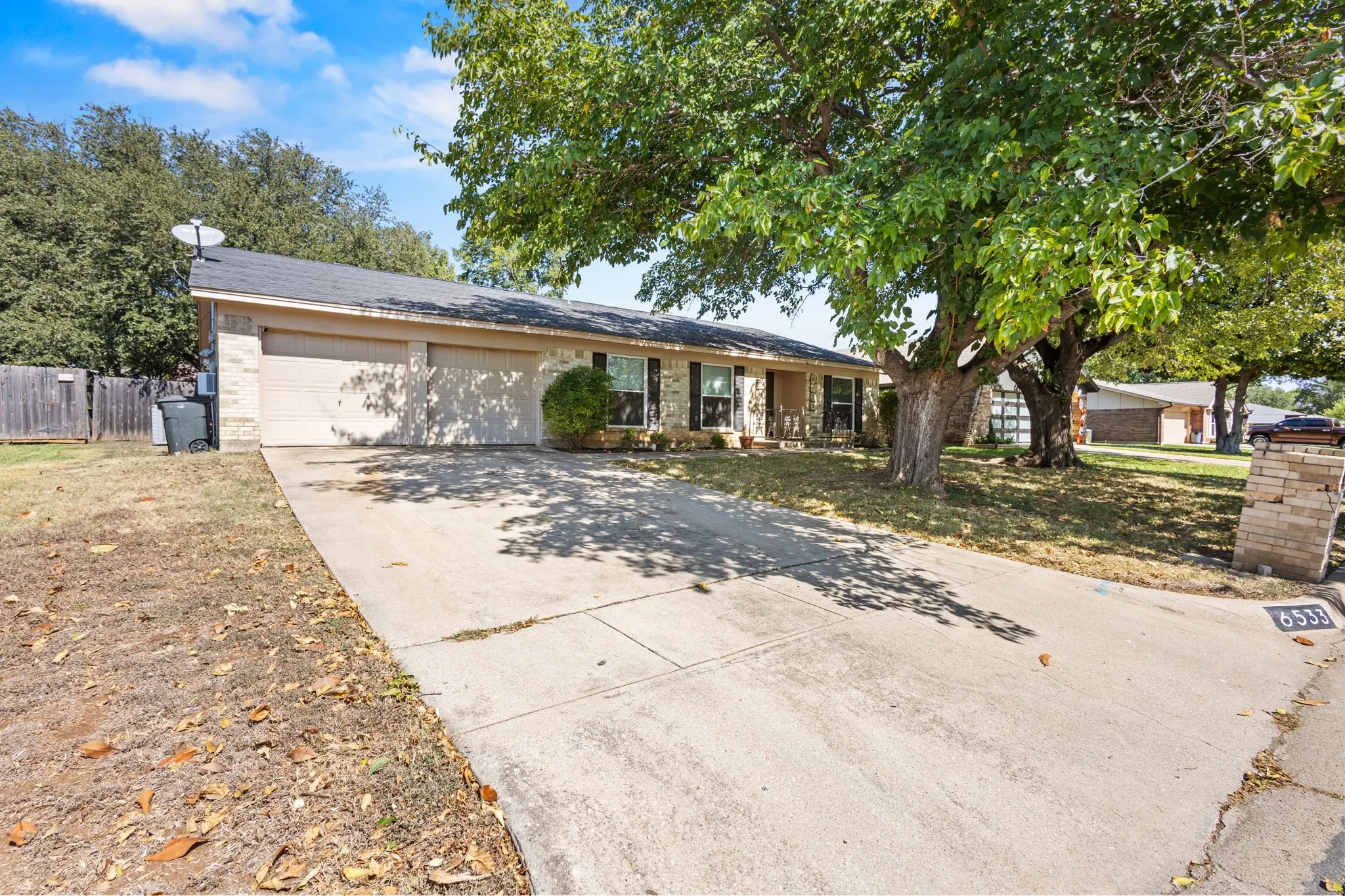 Ranch-style home featuring brick siding, concrete driveway, an attached garage, covered porch, and roof with shingles