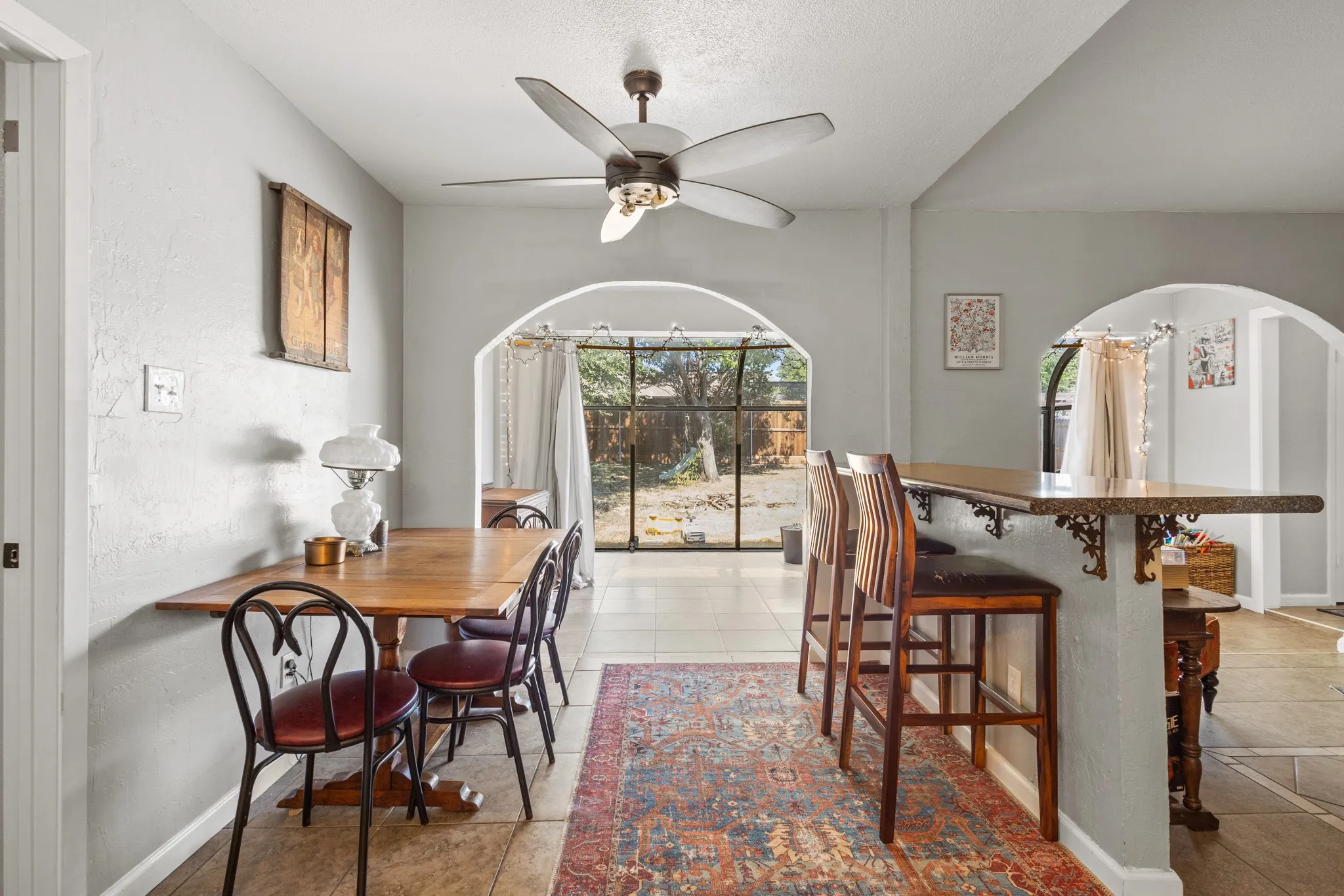 Dining space with arched walkways, light tile patterned floors, a textured wall, and ceiling fan