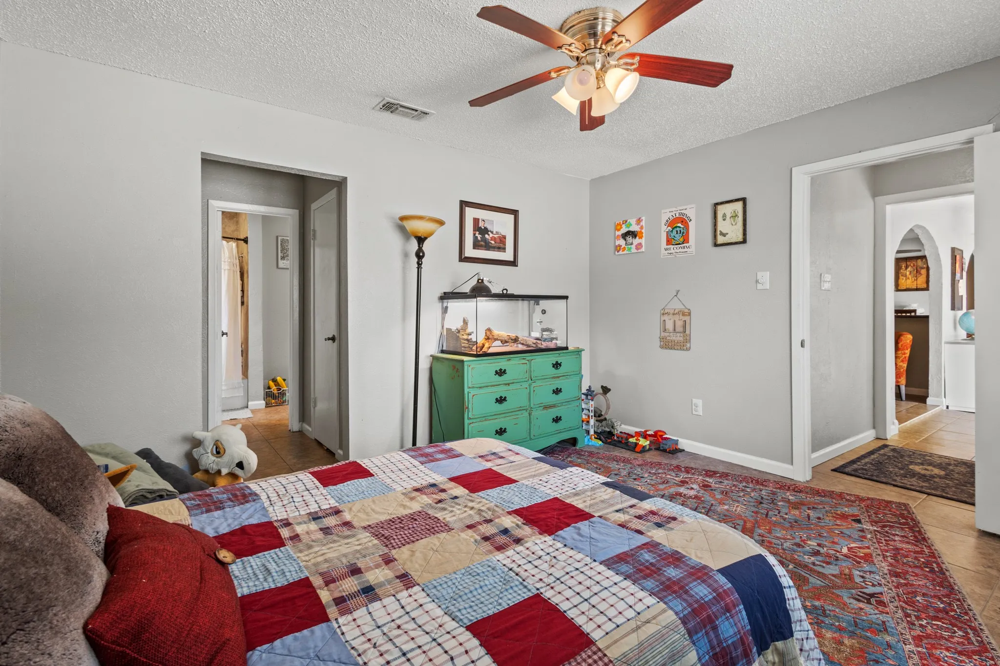 Tiled bedroom with arched walkways, a textured ceiling, and ceiling fan