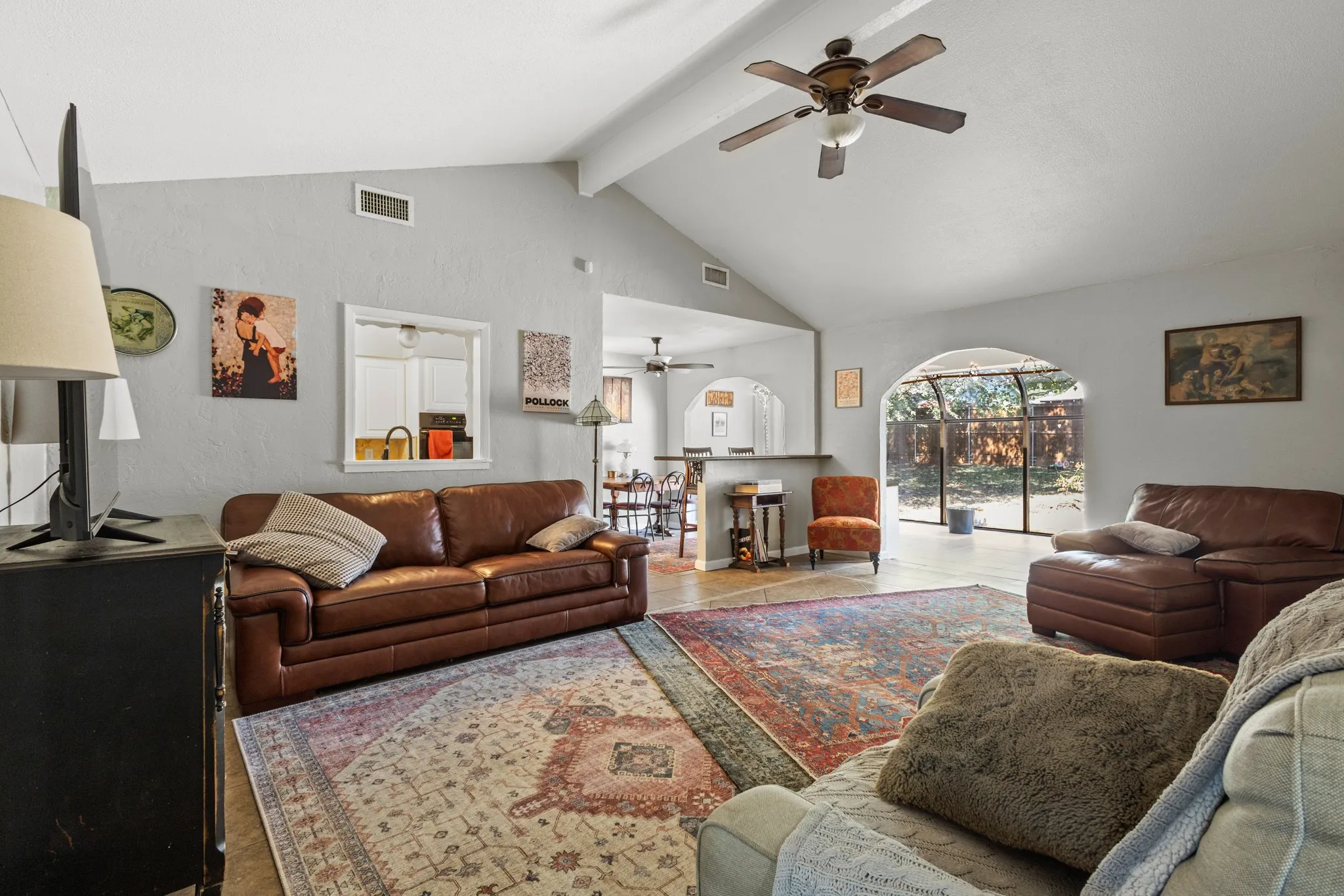 Living area featuring high vaulted ceiling, beamed ceiling, tile patterned floors, and ceiling fan