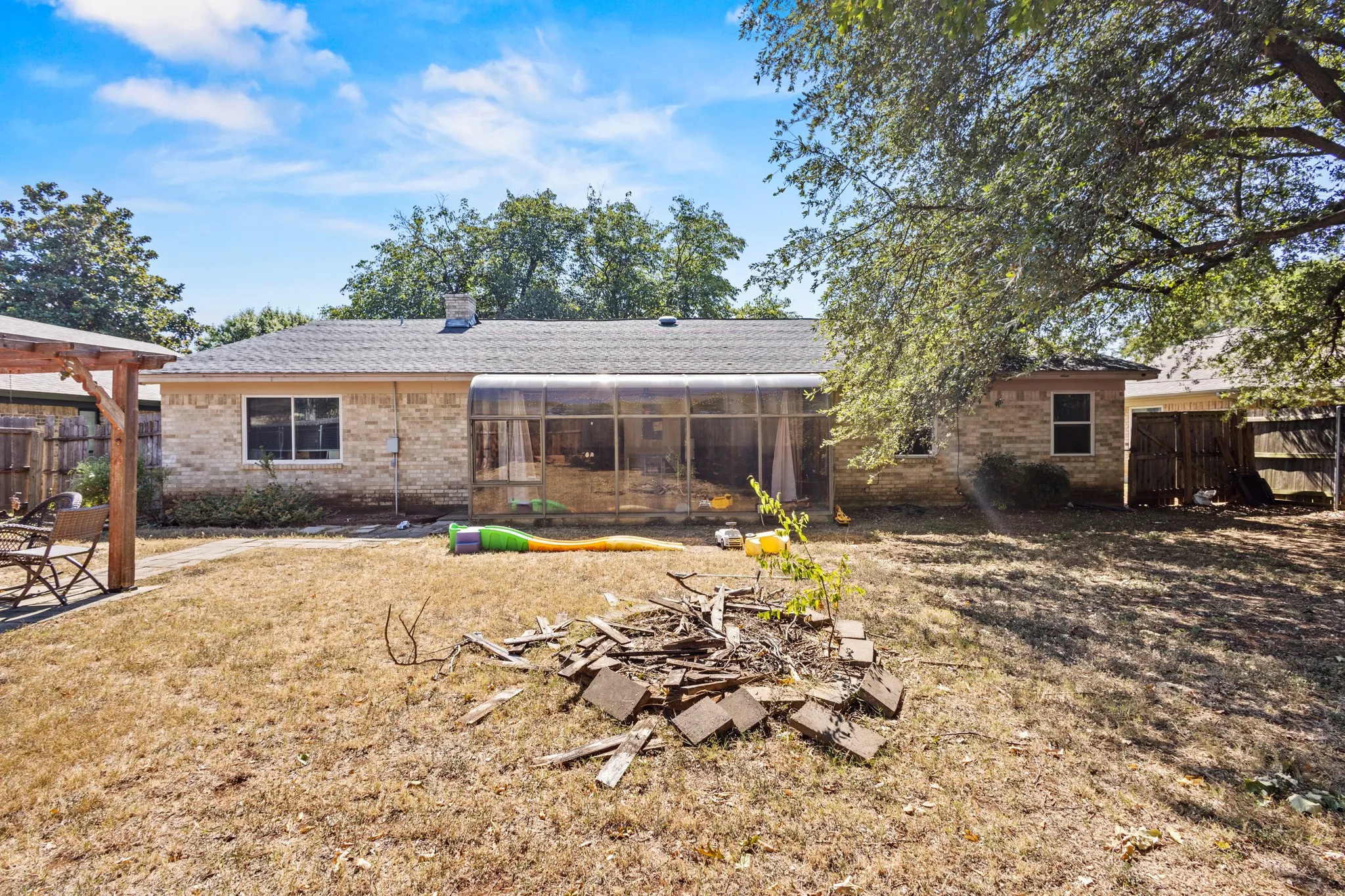 Rear view of house with a fenced backyard, brick siding, a patio area, and a sunroom