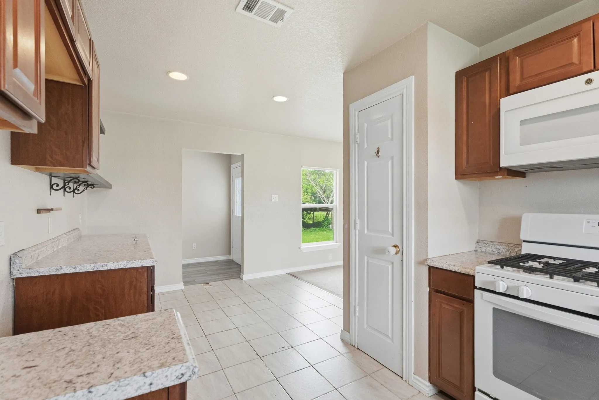 Kitchen with wood cabinetry, light-toned countertops, white tile flooring, and a white gas range