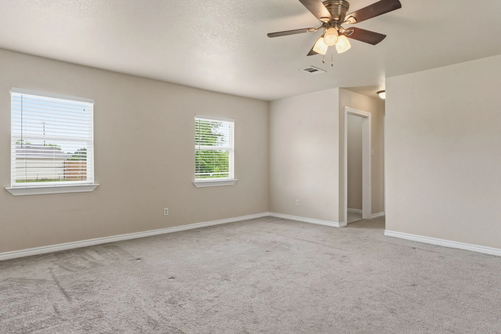 Recessed ceiling fan with integrated lighting, two windows with blinds, light-colored carpeting, and painted walls