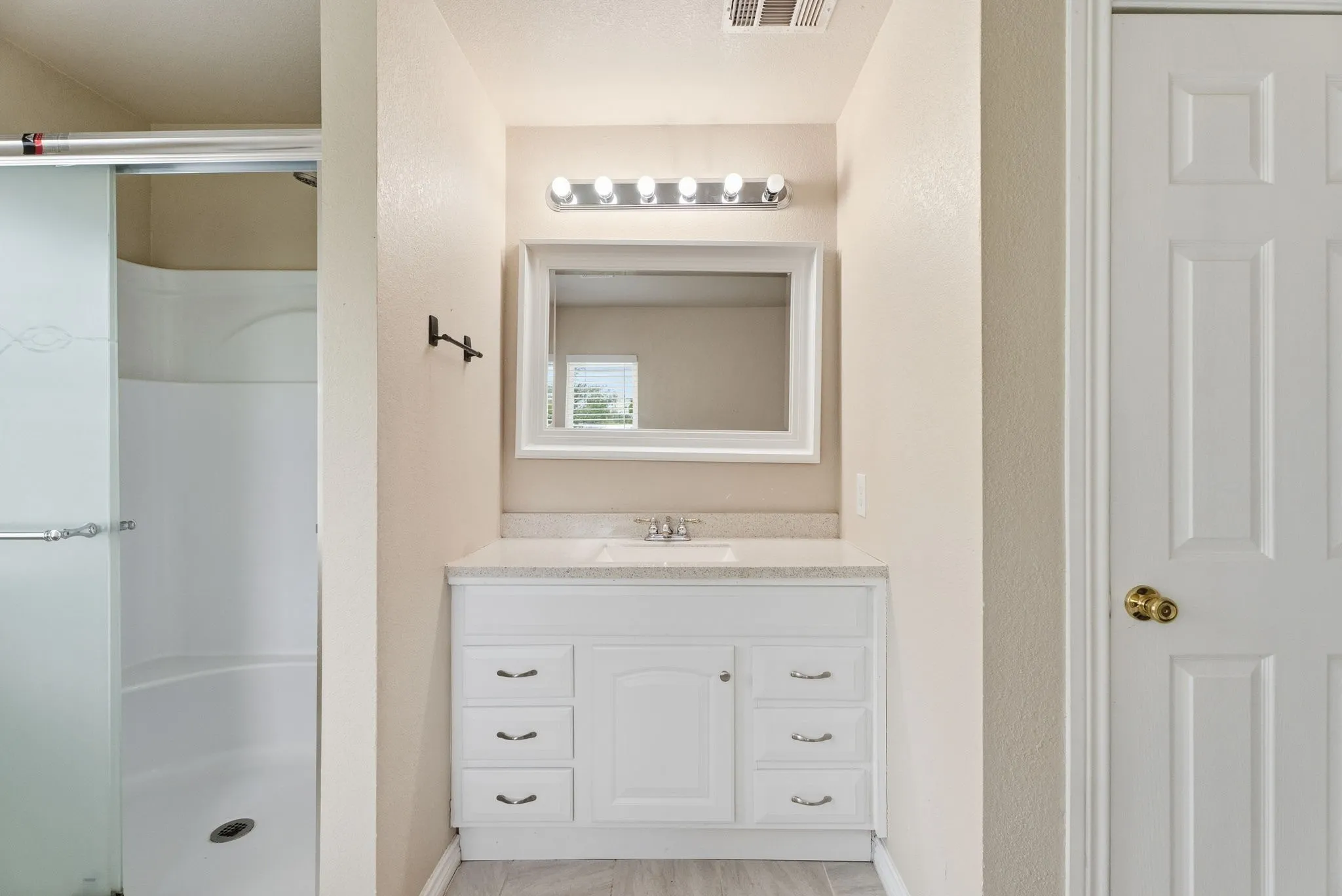 White vanity with a single basin sink, light-toned countertop, and framed mirror