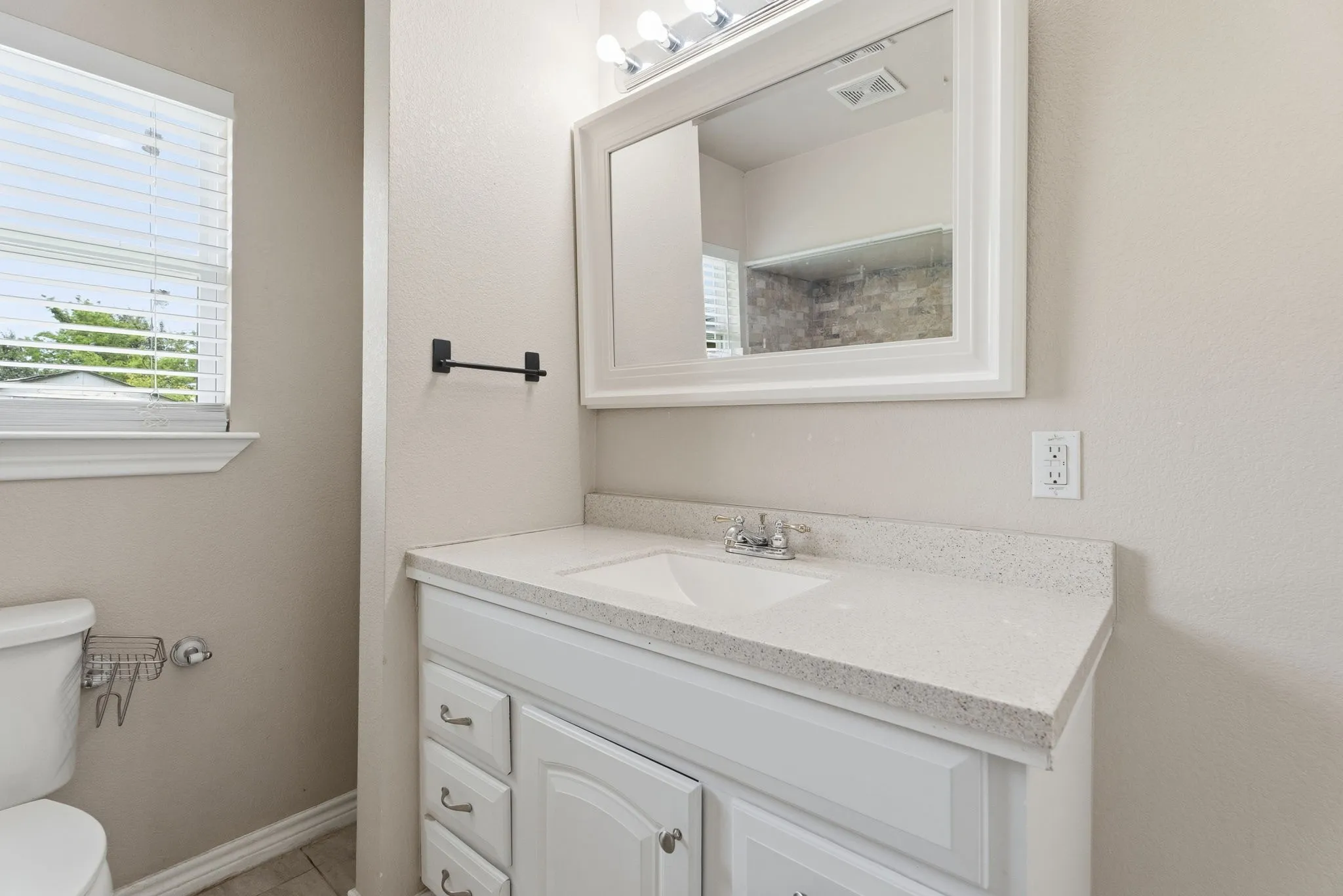White vanity with integrated sink, light-colored countertop, wall-mounted mirror, and overhead vanity lighting