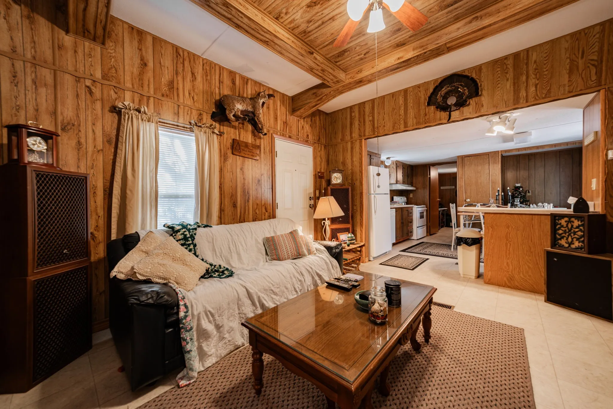 Living area with wooden walls, light tile patterned flooring, a ceiling fan, and a wood ceiling with exposed beams