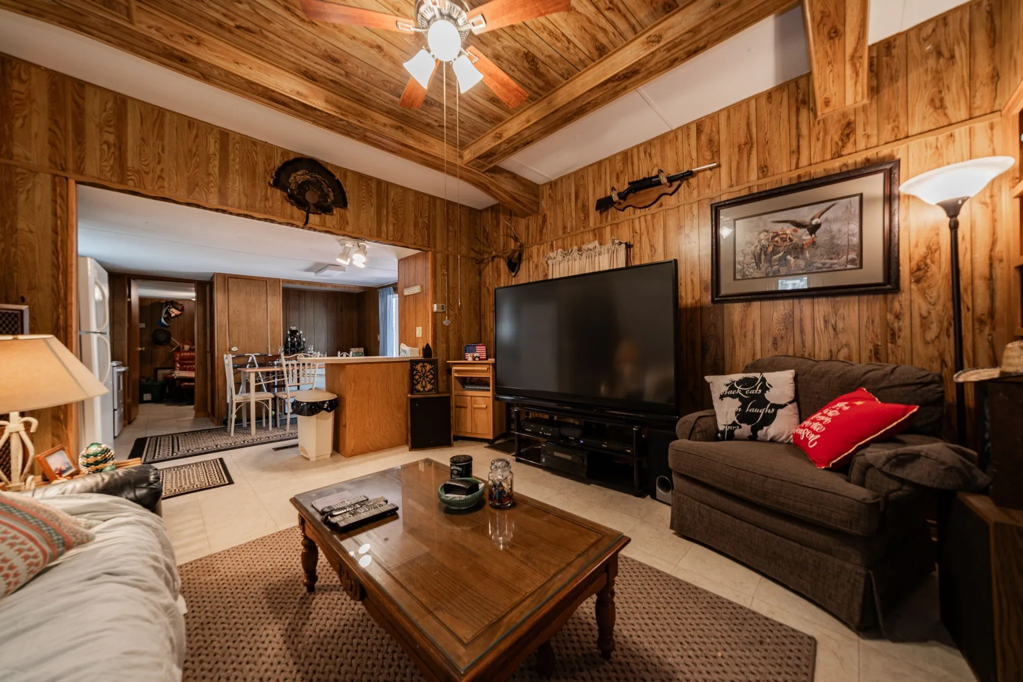 Living area featuring wooden walls, light tile patterned flooring, ceiling fan, and a wooden ceiling with exposed beams