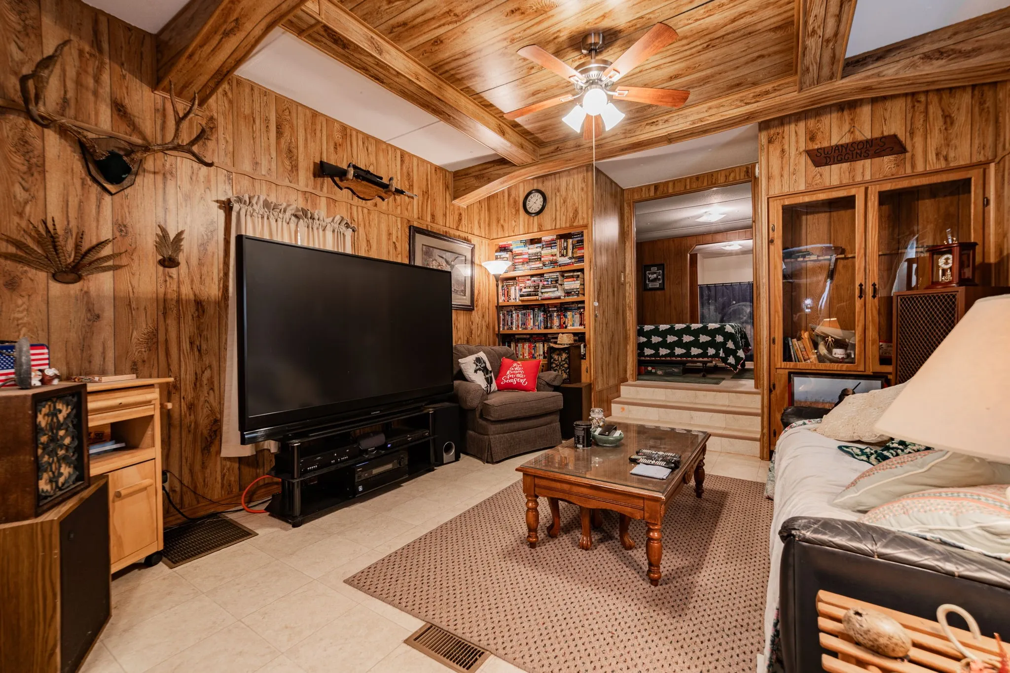 Living room featuring wood walls, beam ceiling, and ceiling fan
