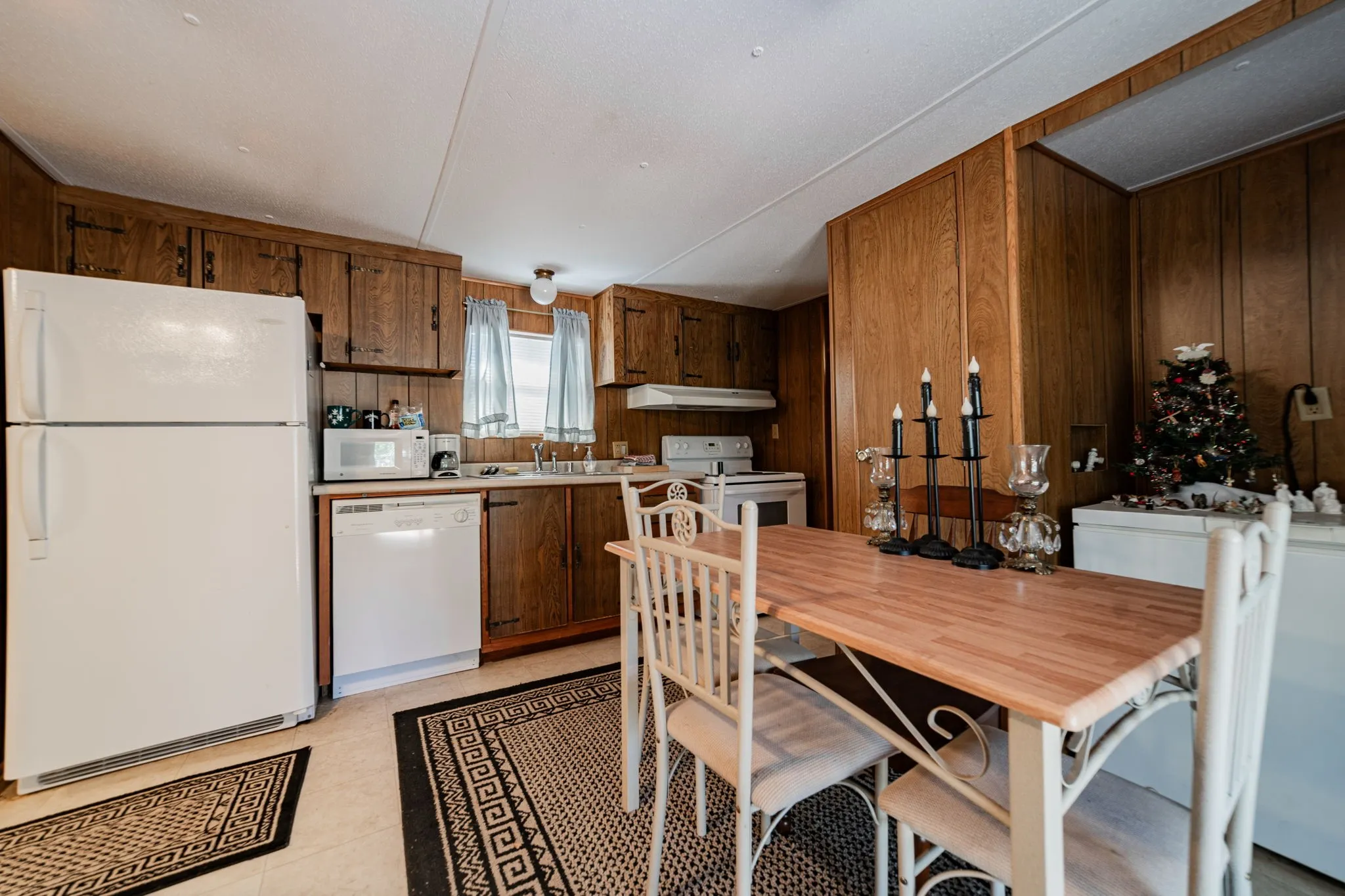 Kitchen with white appliances, light countertops, light tile patterned floors, wooden walls, and under cabinet range hood