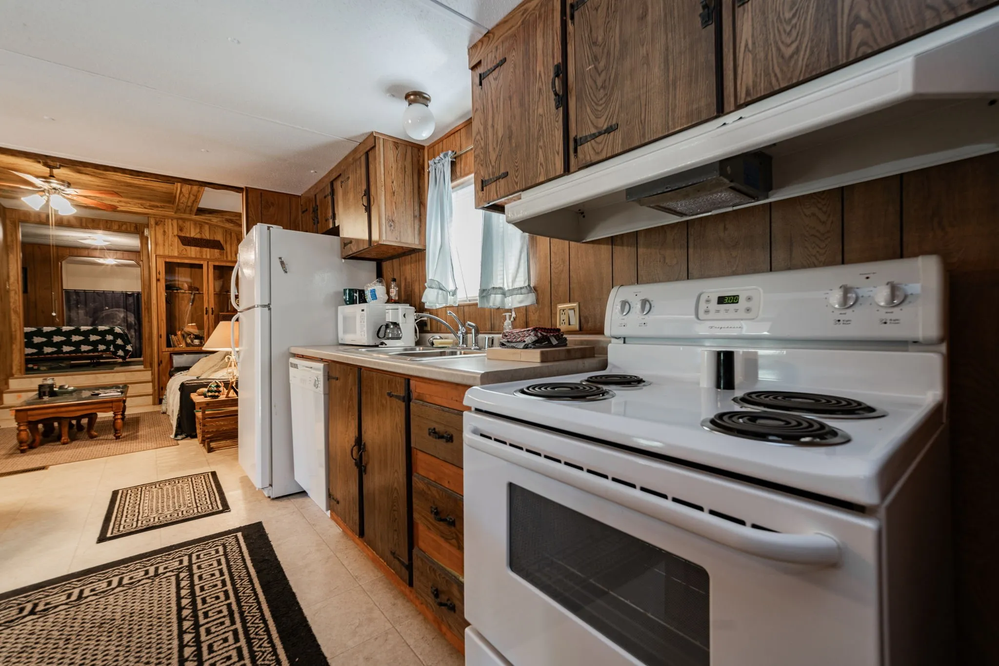 Kitchen with under cabinet range hood, white appliances, wooden walls, light countertops, and light tile patterned flooring