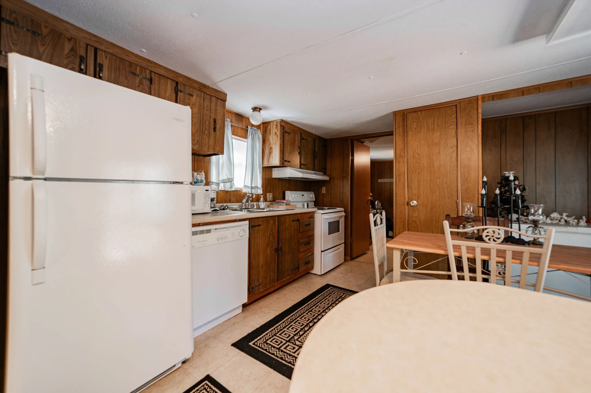 Kitchen featuring white appliances, light countertops, wooden walls, under cabinet range hood, and light tile patterned floors