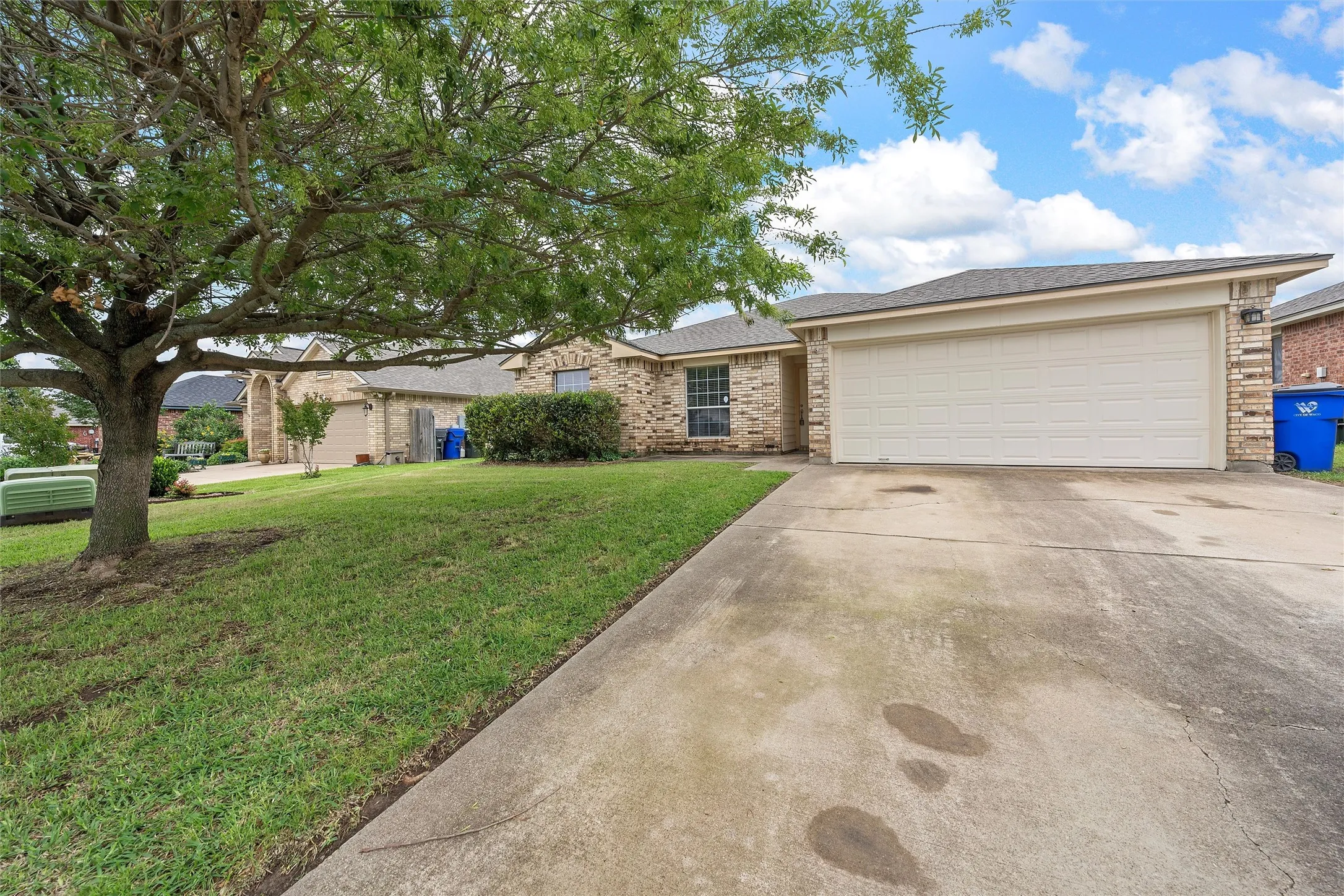 Single story home featuring concrete driveway, a front yard, a garage, brick siding, and roof with shingles