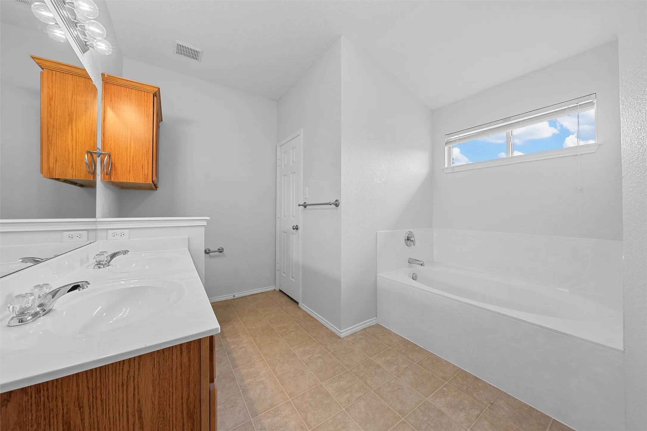 Bathroom featuring a bath, double vanity, light tile patterned floors, and lofted ceiling