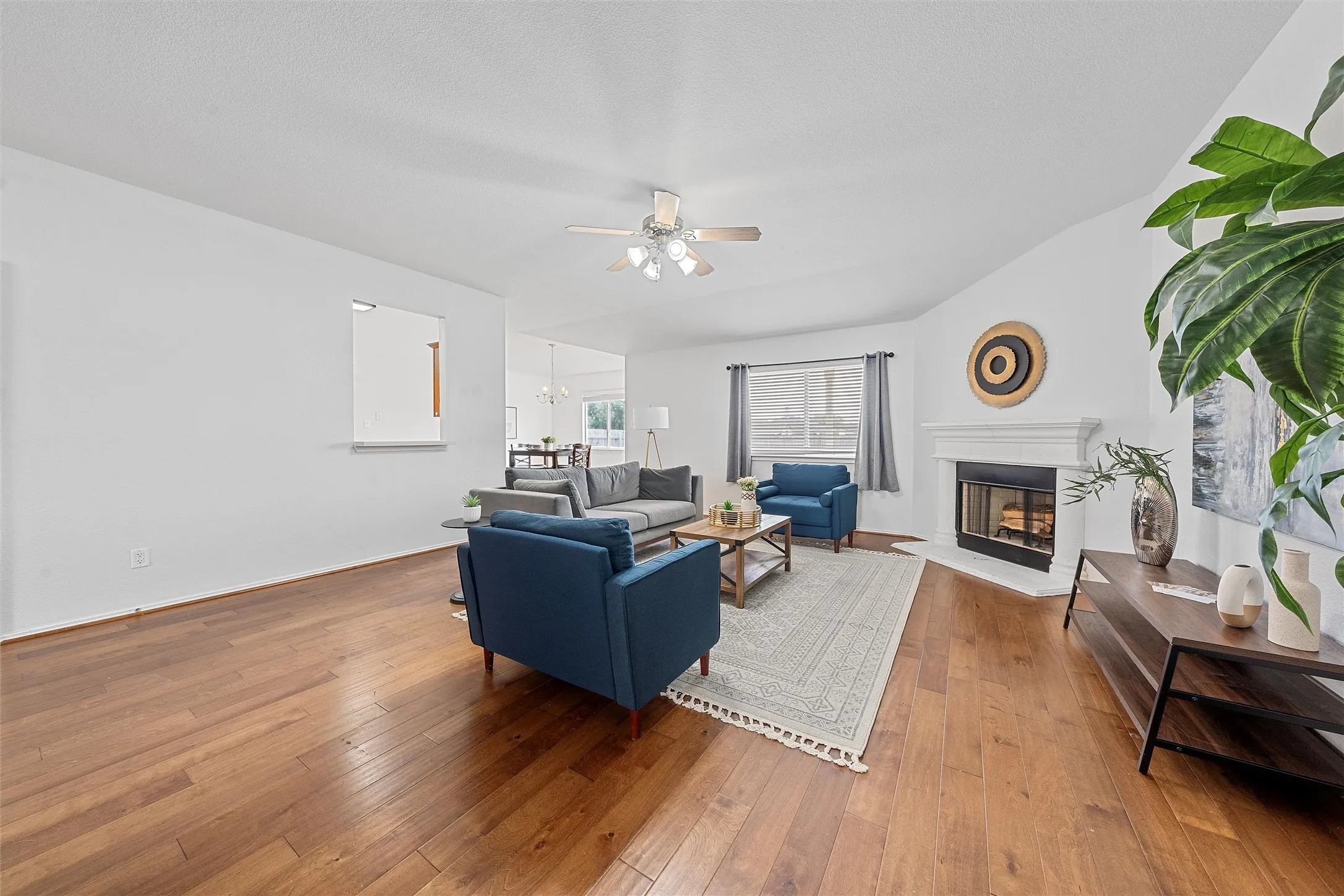 Living room with hardwood / wood-style floors, a fireplace with raised hearth, a ceiling fan, and a chandelier