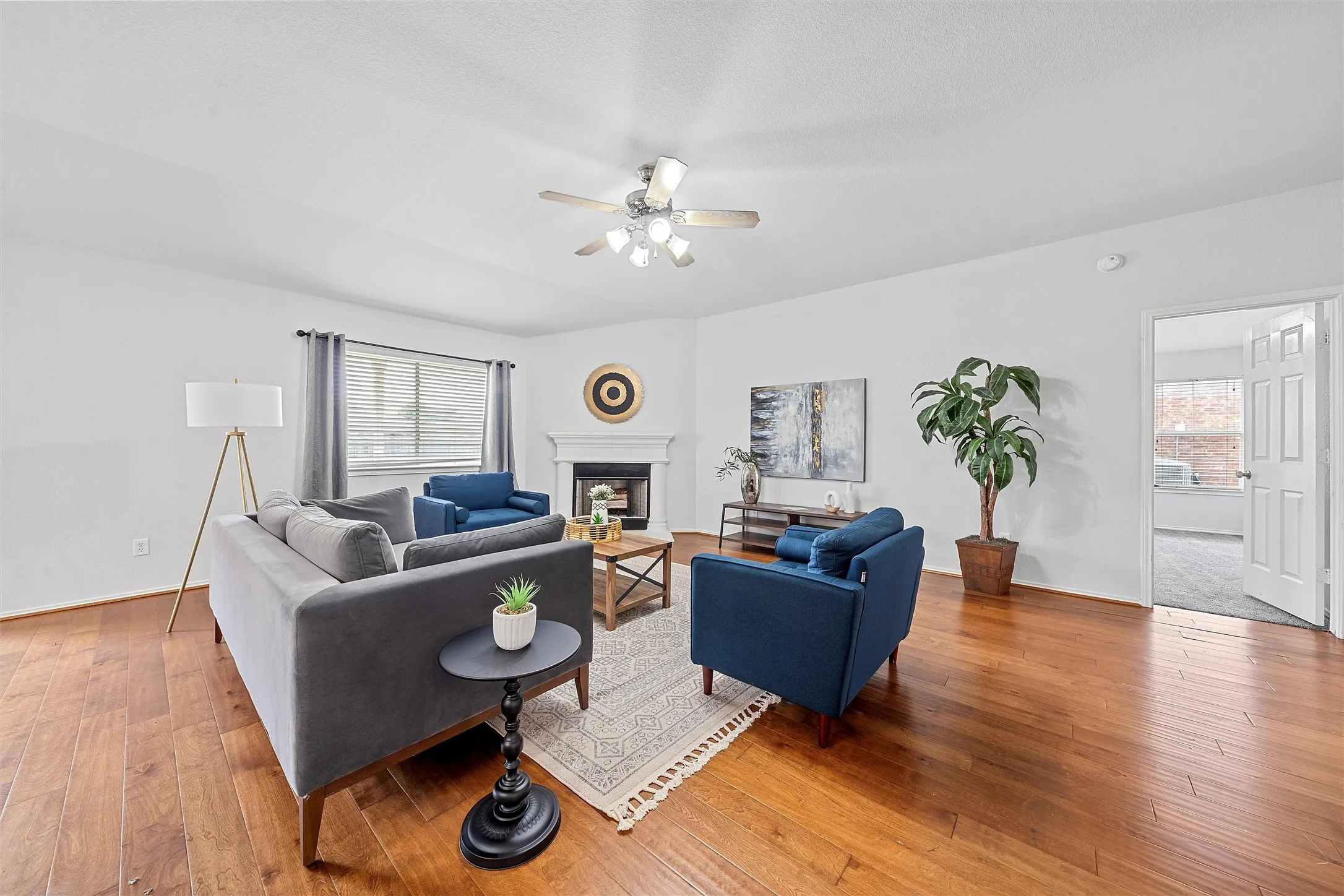 Living area with light wood-style floors, a glass covered fireplace, and ceiling fan