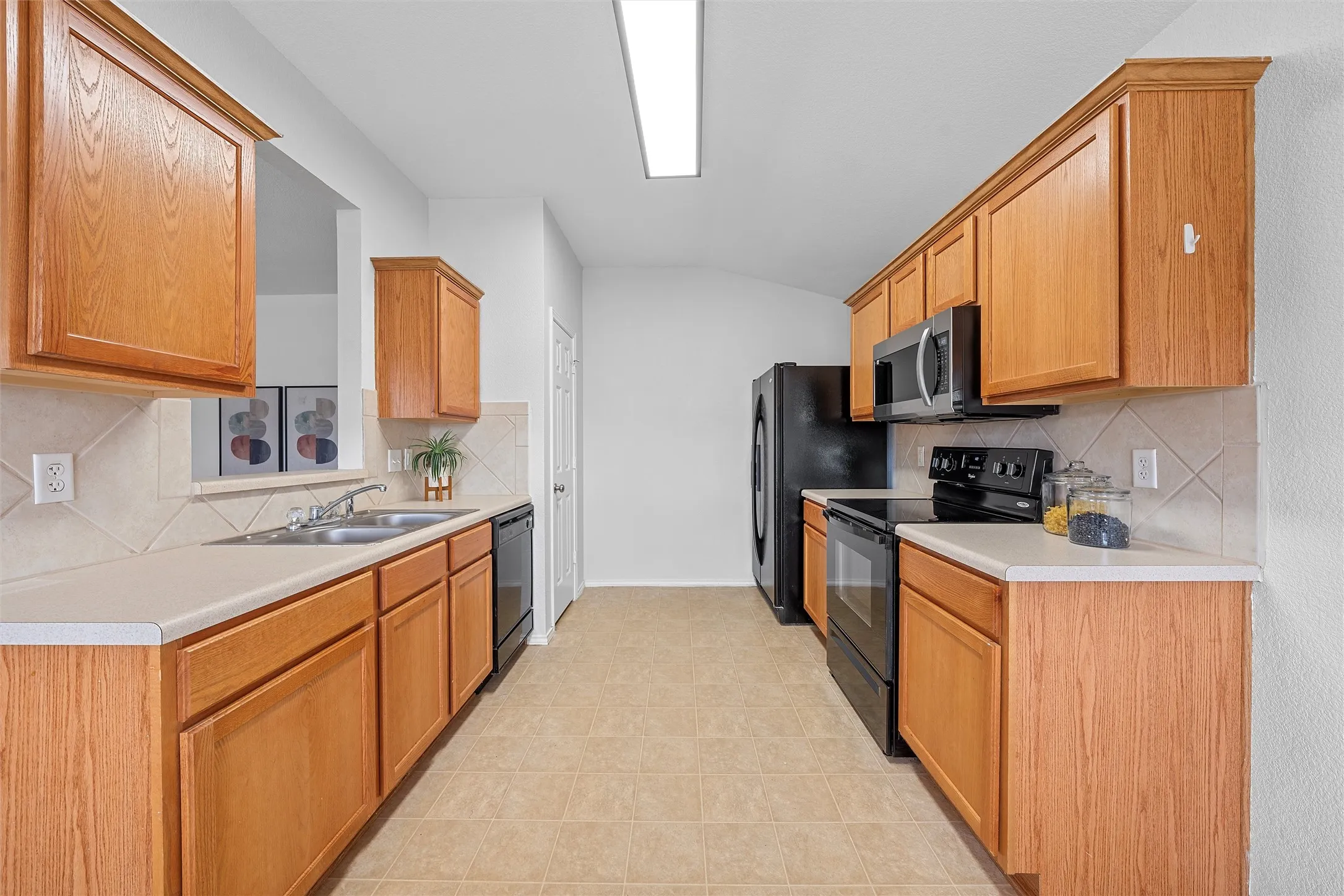 Kitchen with backsplash, black appliances, light countertops, lofted ceiling, and brown cabinets