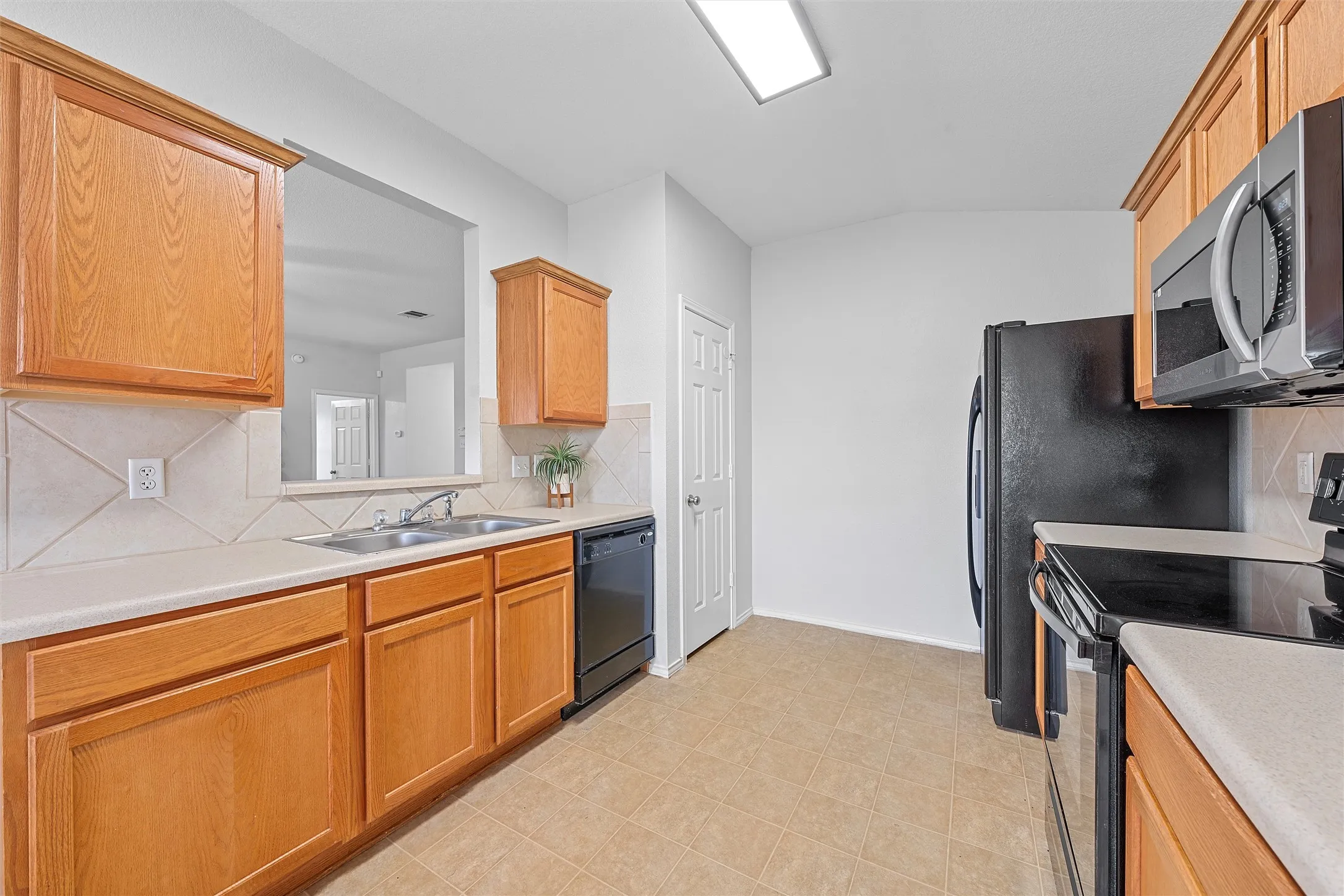 Kitchen featuring decorative backsplash, electric range, light countertops, stainless steel microwave, and black dishwasher