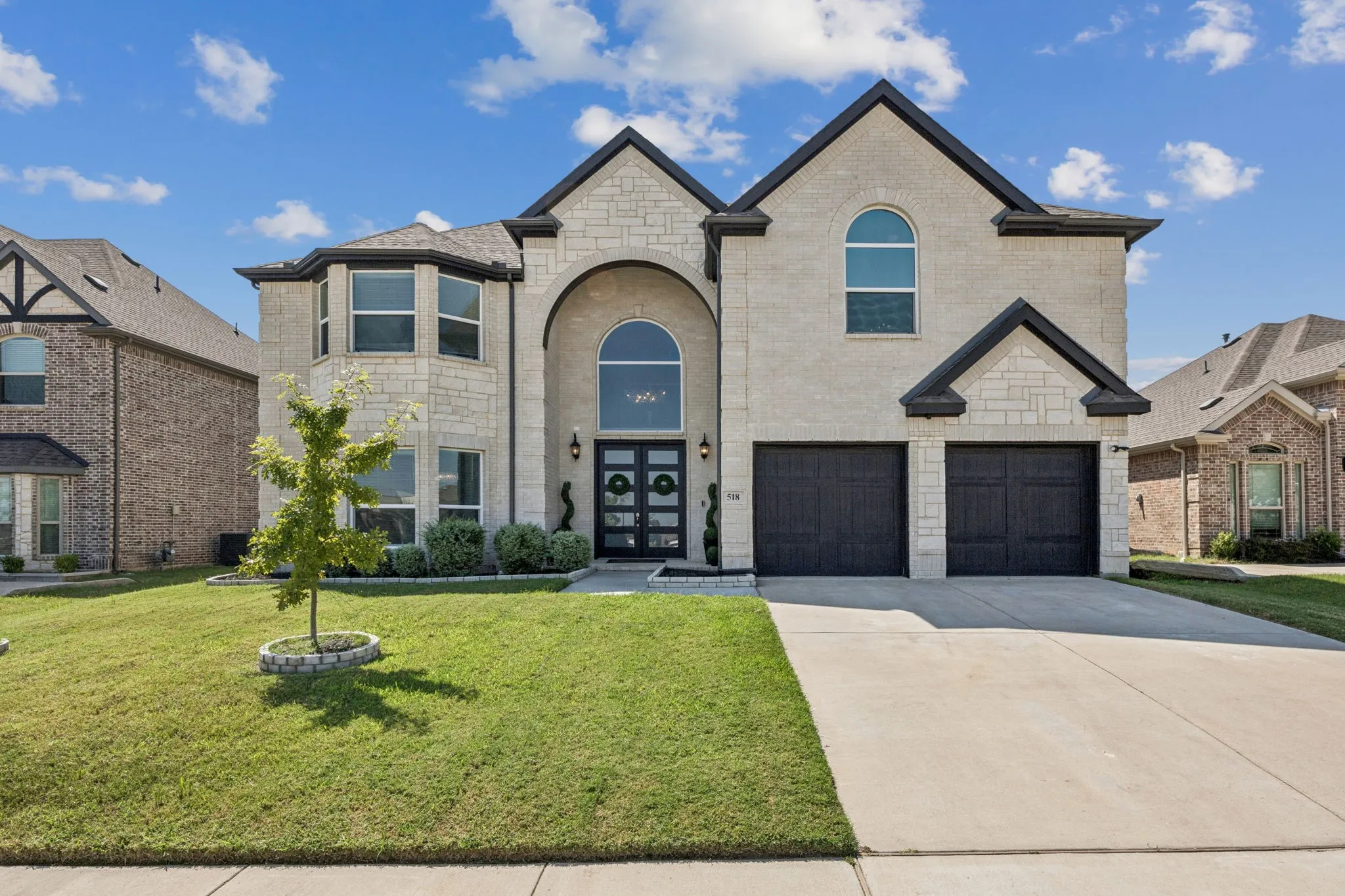 French country home featuring concrete driveway, a front lawn, stone siding, brick siding, and an attached garage