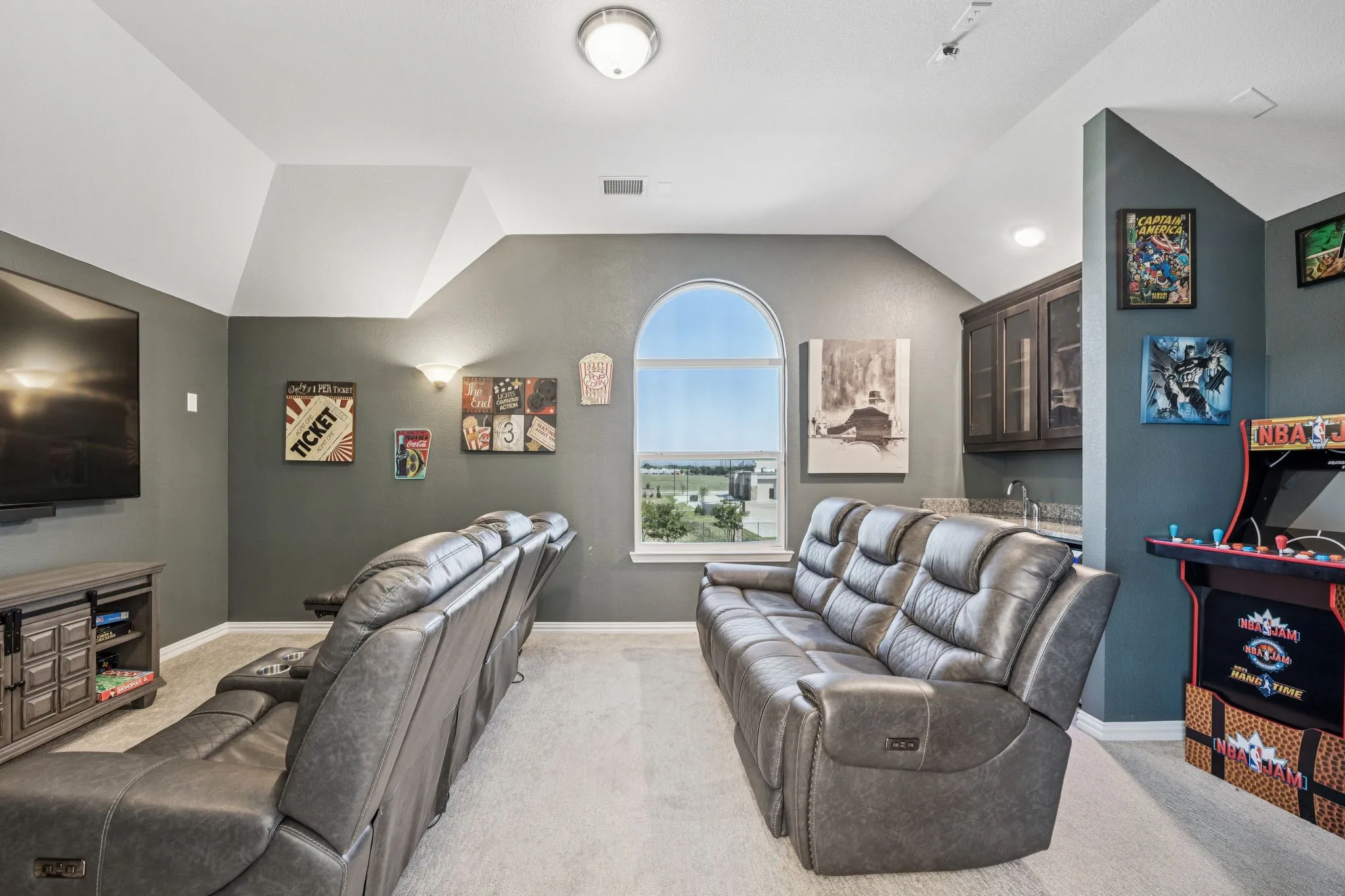 Cinema room featuring vaulted ceiling, light colored carpet, and wet bar
