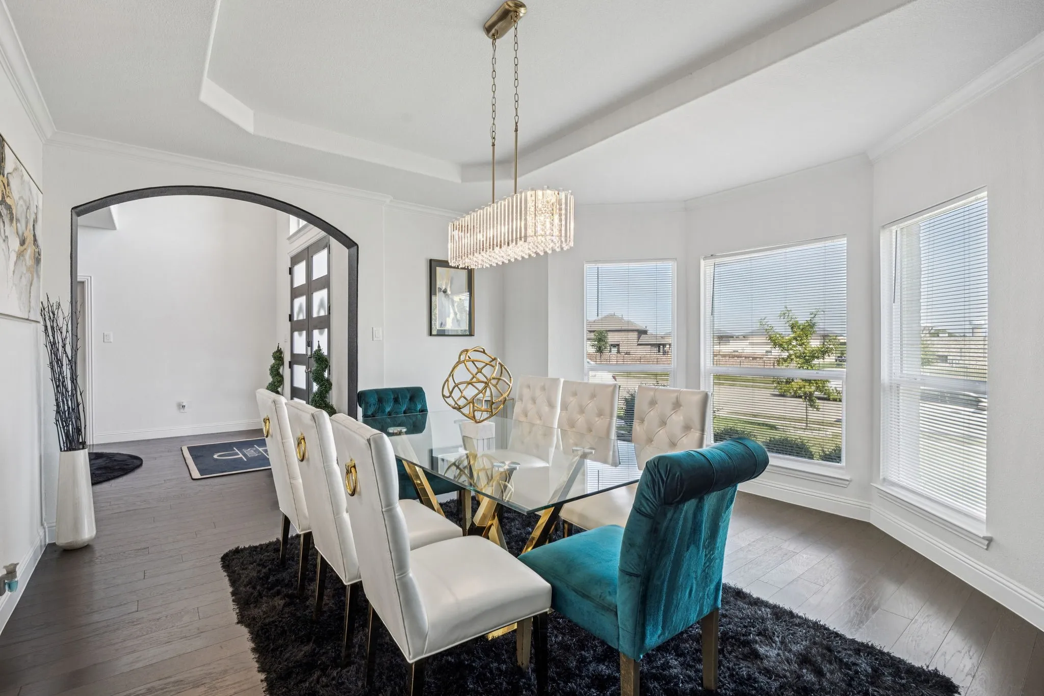 Dining space featuring crown molding, dark wood-style flooring, arched walkways, a raised ceiling, and a chandelier