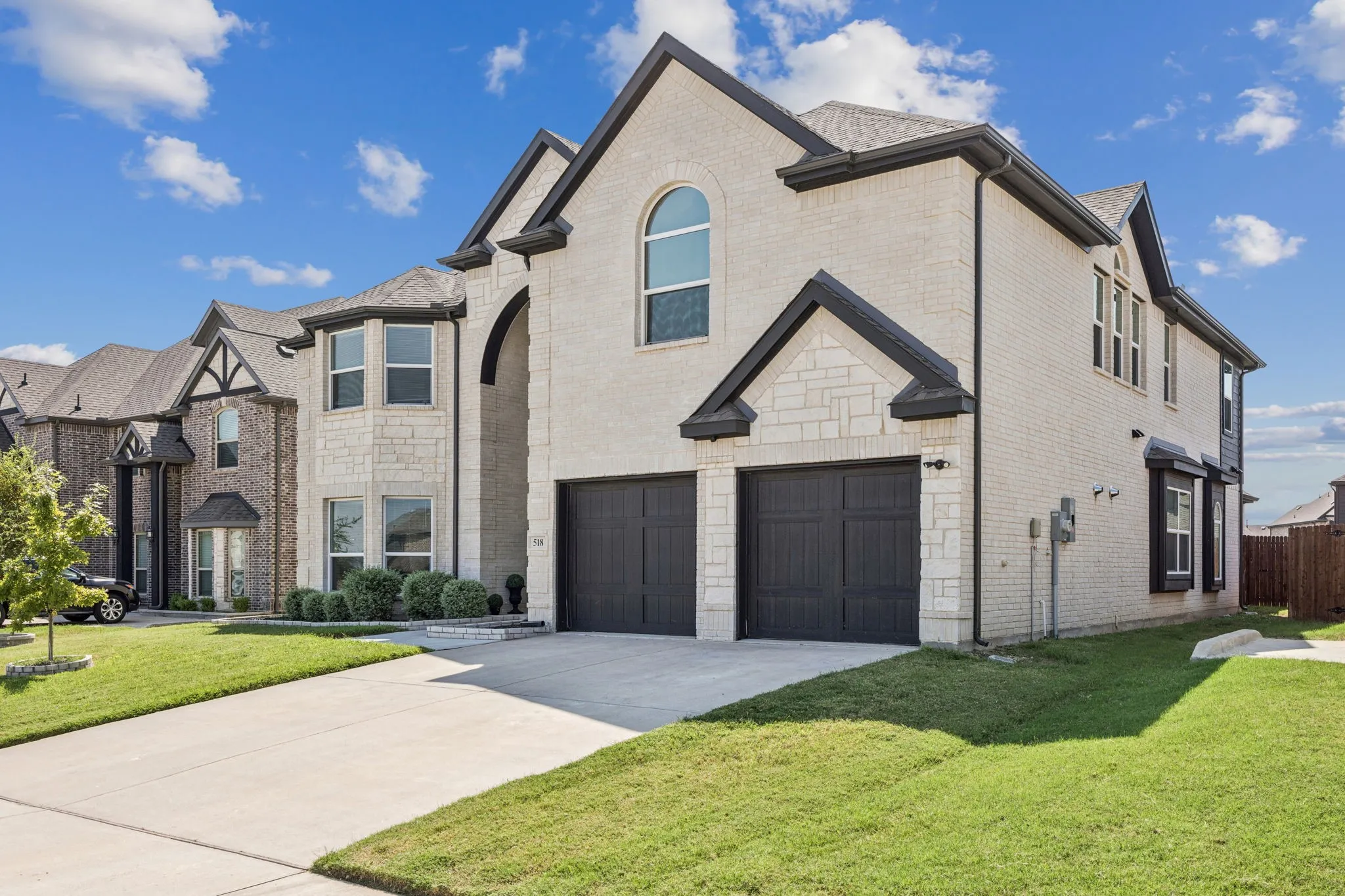 French country inspired facade with brick siding, a front yard, a garage, concrete driveway, and stone siding