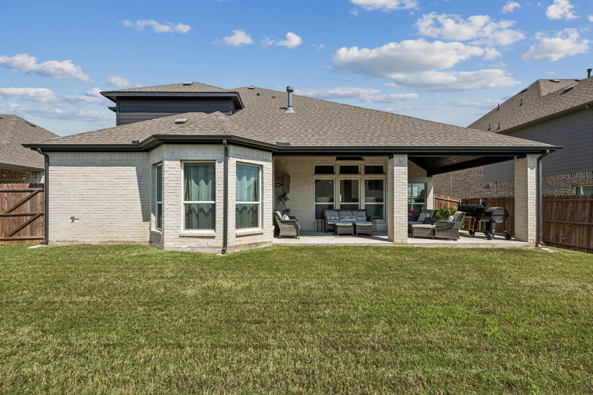 Rear view of house featuring outdoor lounge area, a fenced backyard, roof with shingles, a patio area, and brick siding