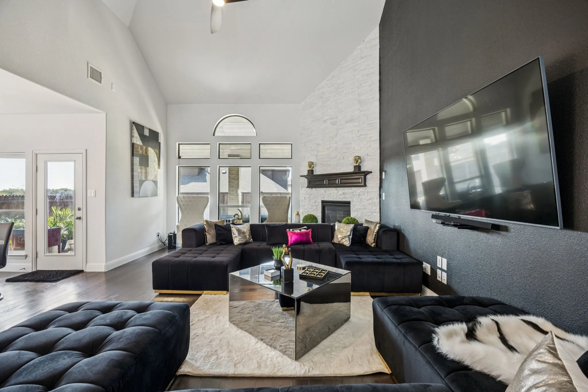 Living room featuring high vaulted ceiling, wood finished floors, a stone fireplace, and ceiling fan