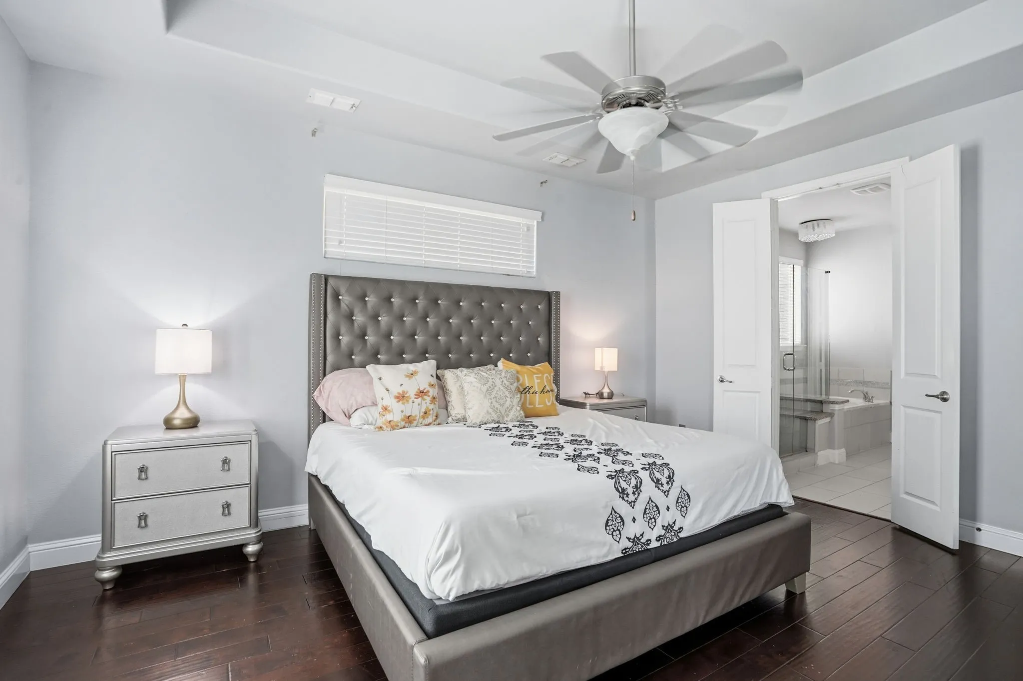 Bedroom with dark wood-style floors, ensuite bath, a ceiling fan, and a raised ceiling