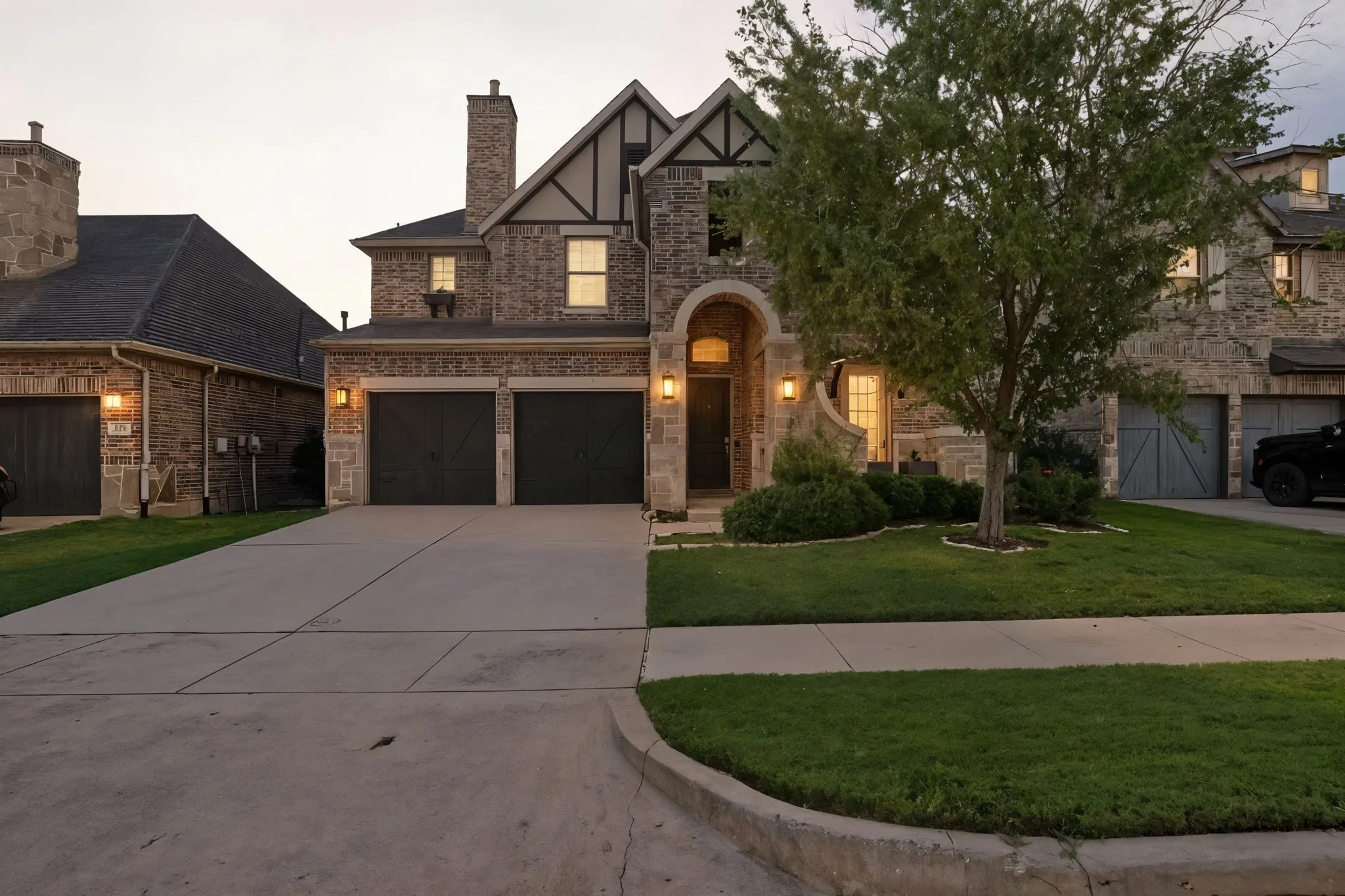 Tudor-style house featuring a front yard, concrete driveway, a chimney, a garage, and stucco siding