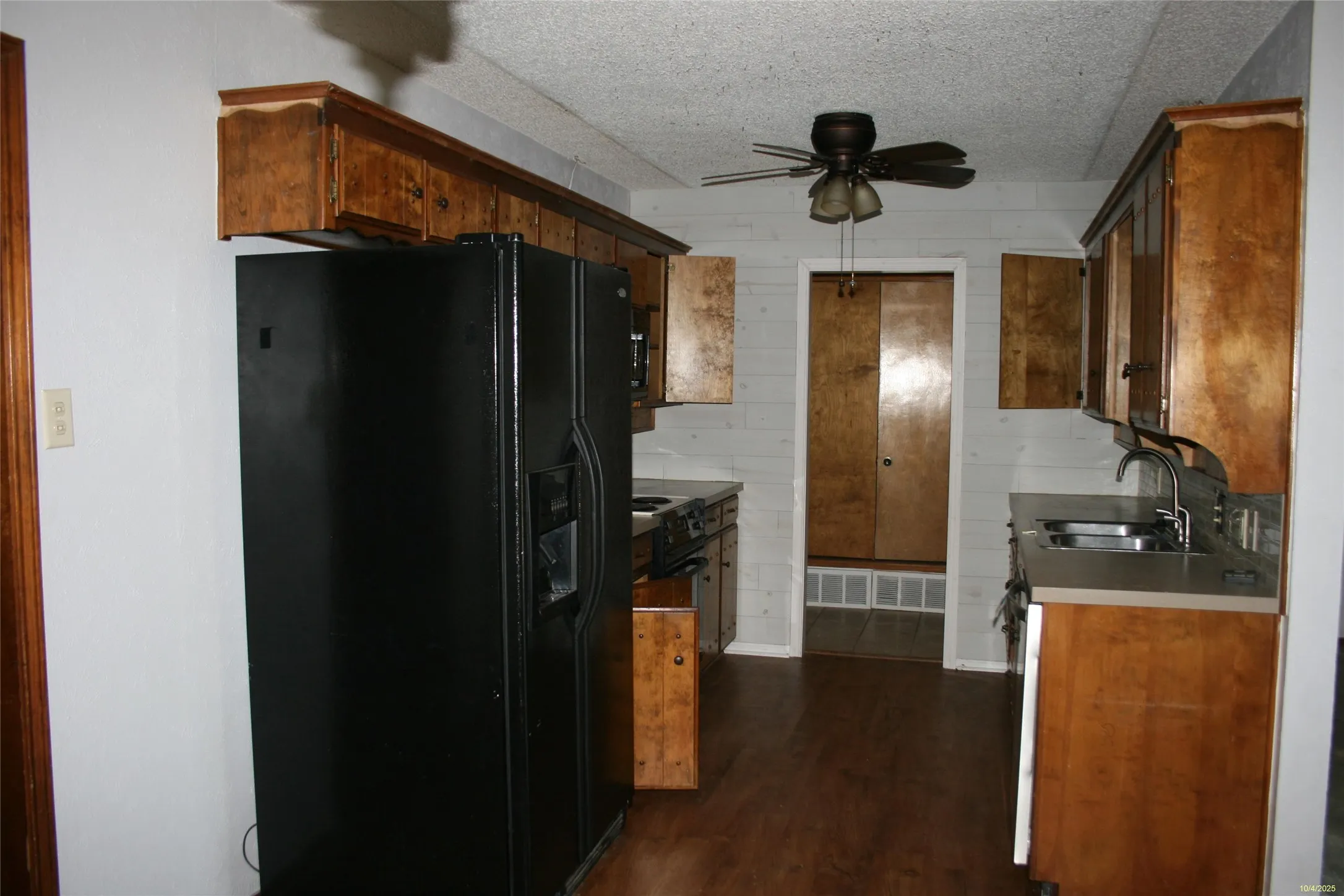 Kitchen with black fridge with ice dispenser, dark wood-style flooring, a textured ceiling, a ceiling fan, and wooden walls